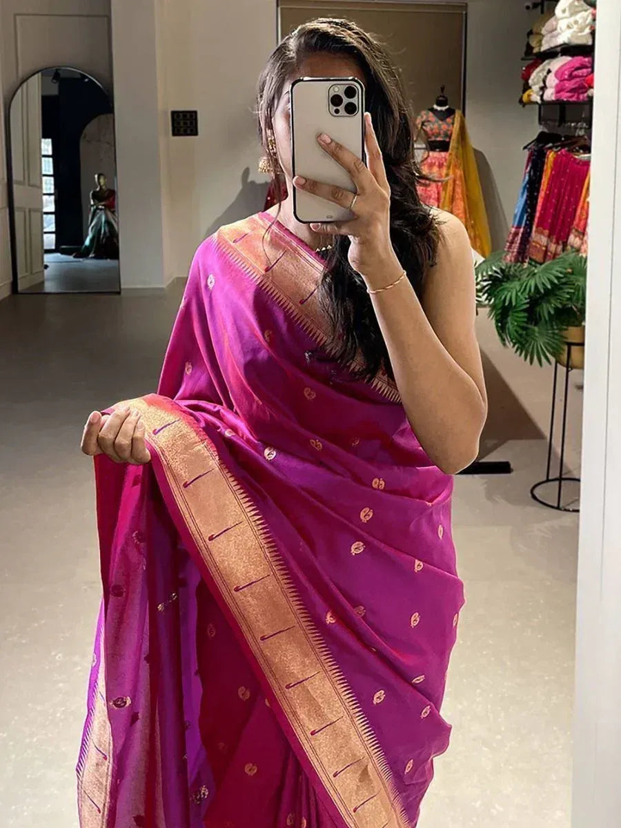 Woman wearing vibrant purple Indian saree with gold border, taking mirror selfie in boutique