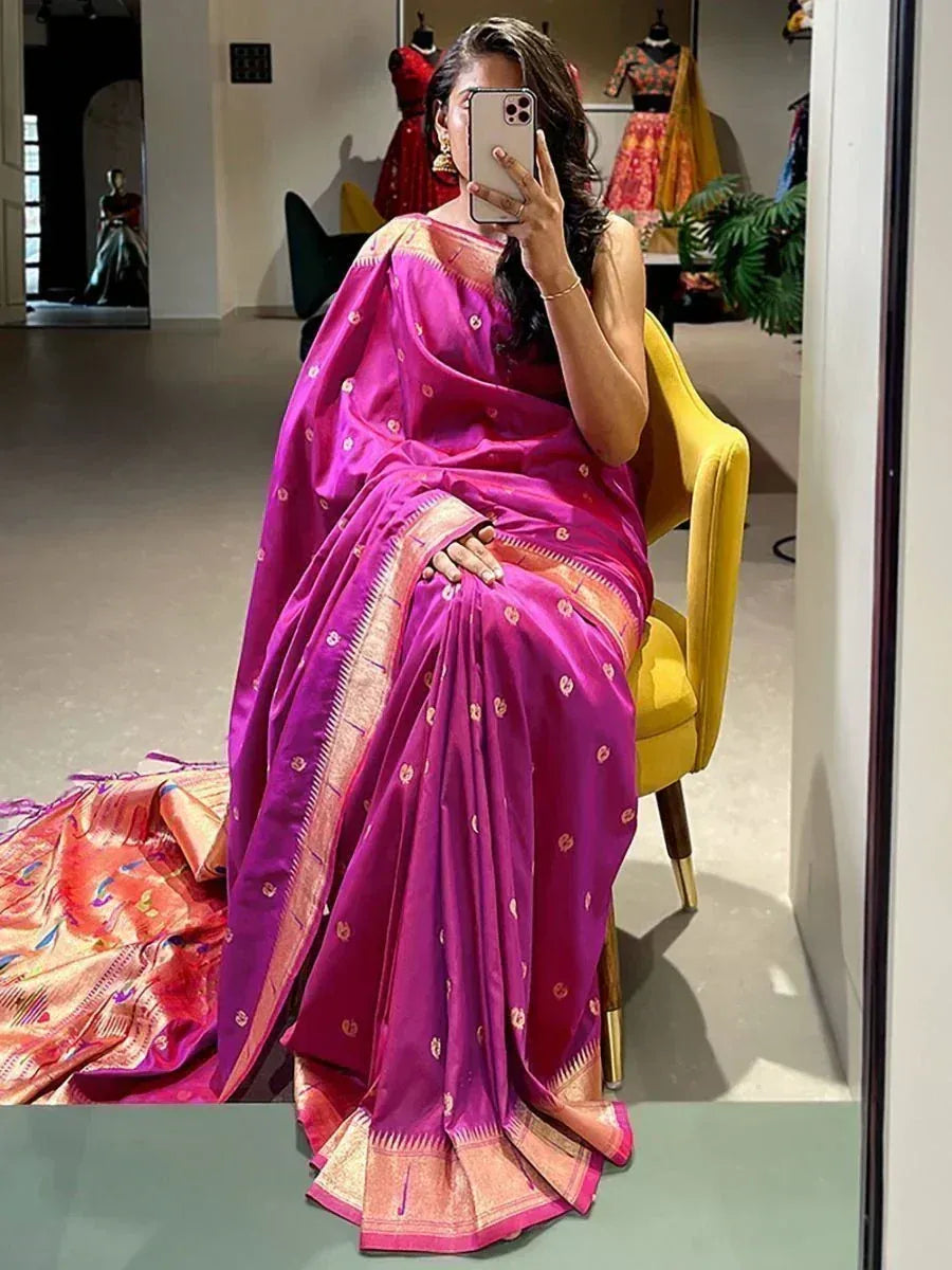 Woman in vibrant pink silk saree with gold motifs, taking mirror selfie in boutique