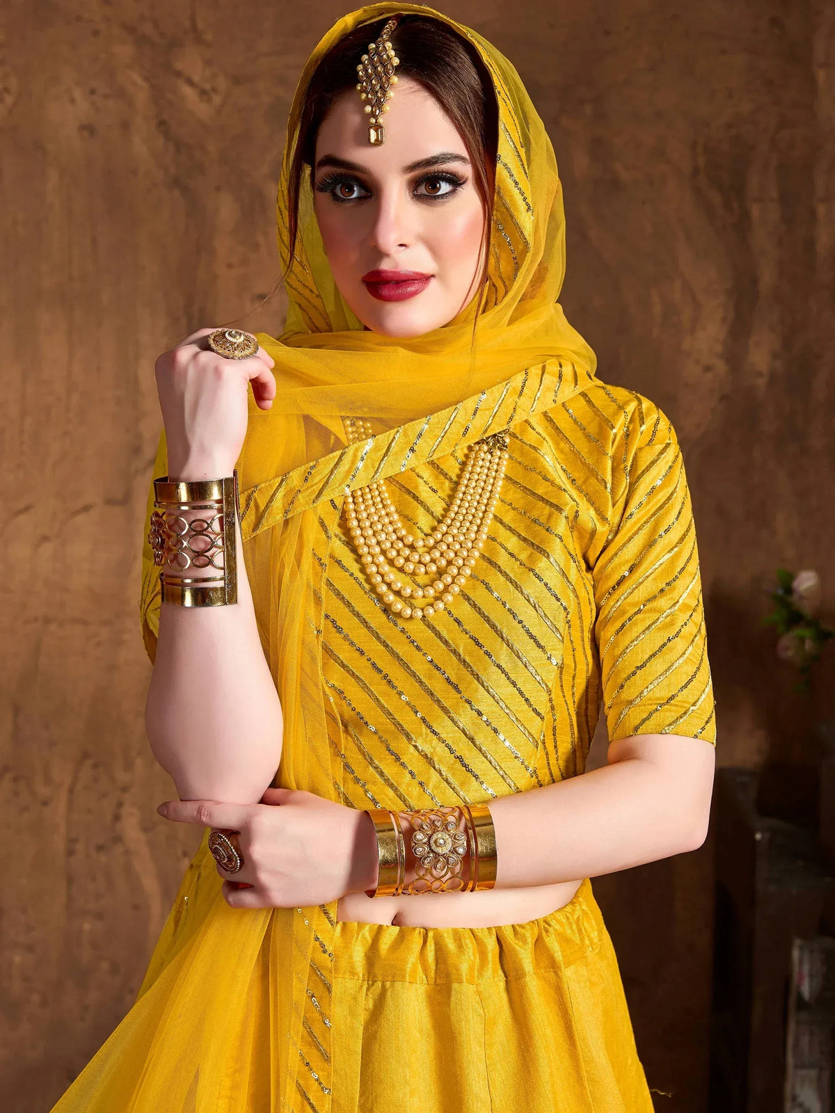 Woman in a yellow designer ethnic salwar kameez with gold stripes, pearl necklace, and jewelry