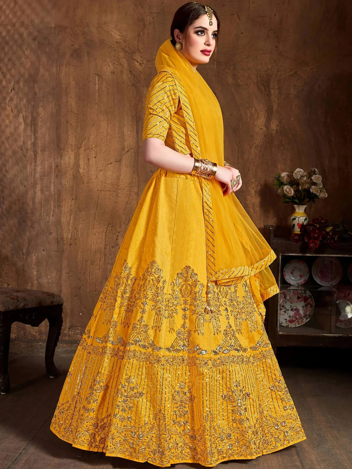 Woman wearing a yellow designer lehenga choli with intricate gold embroidery and a matching dupatta