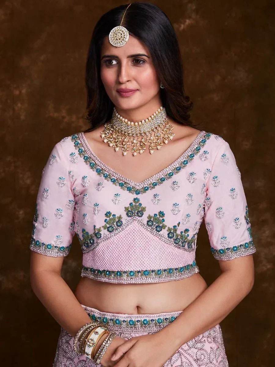 Pink embroidered lehenga choli with blue floral motifs and gold jewelry, perfect for Indian ethnic wear