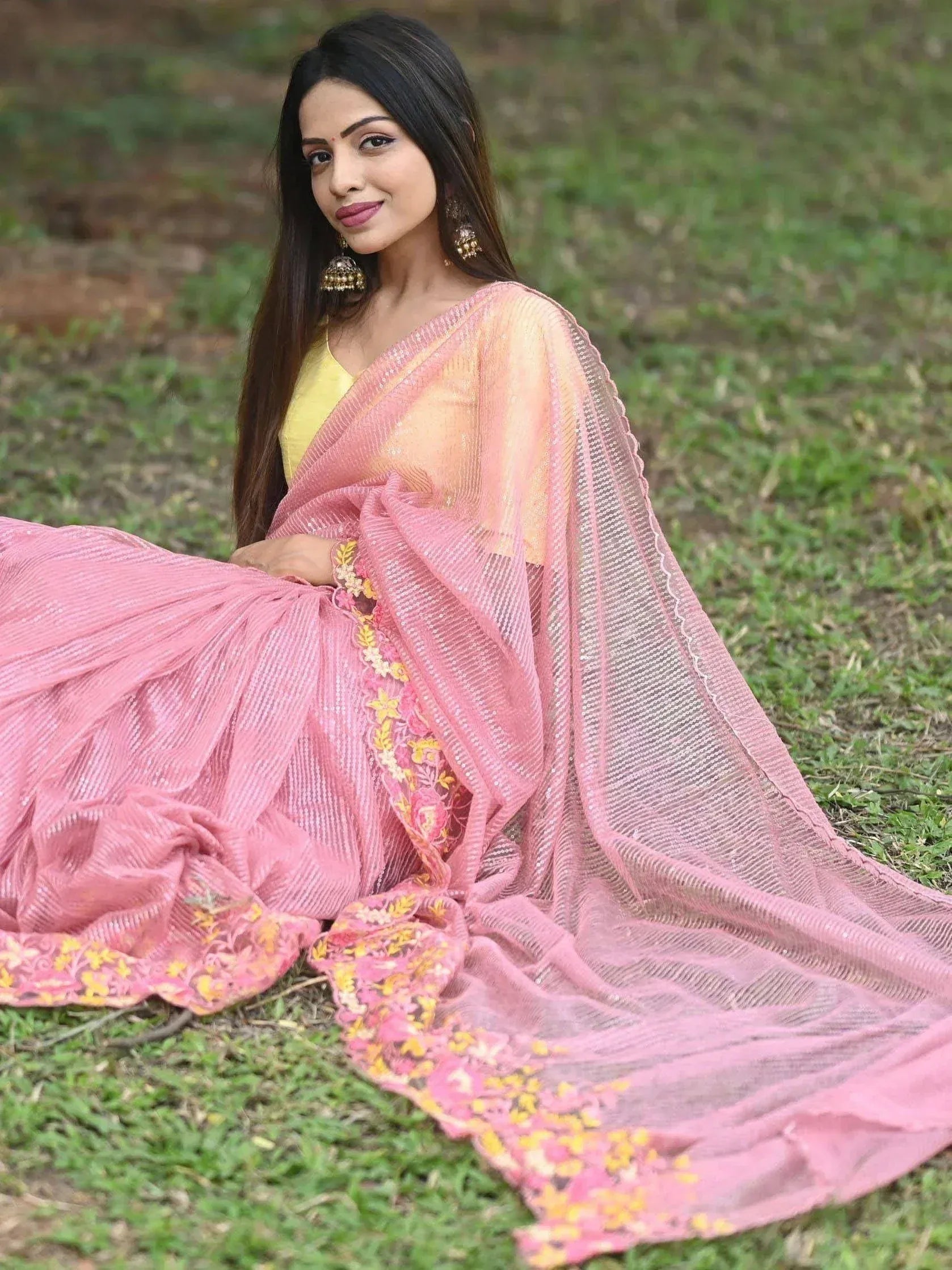 Woman in pink embroidered lehenga choli with yellow blouse, sitting on grass, Indian ethnic wear
