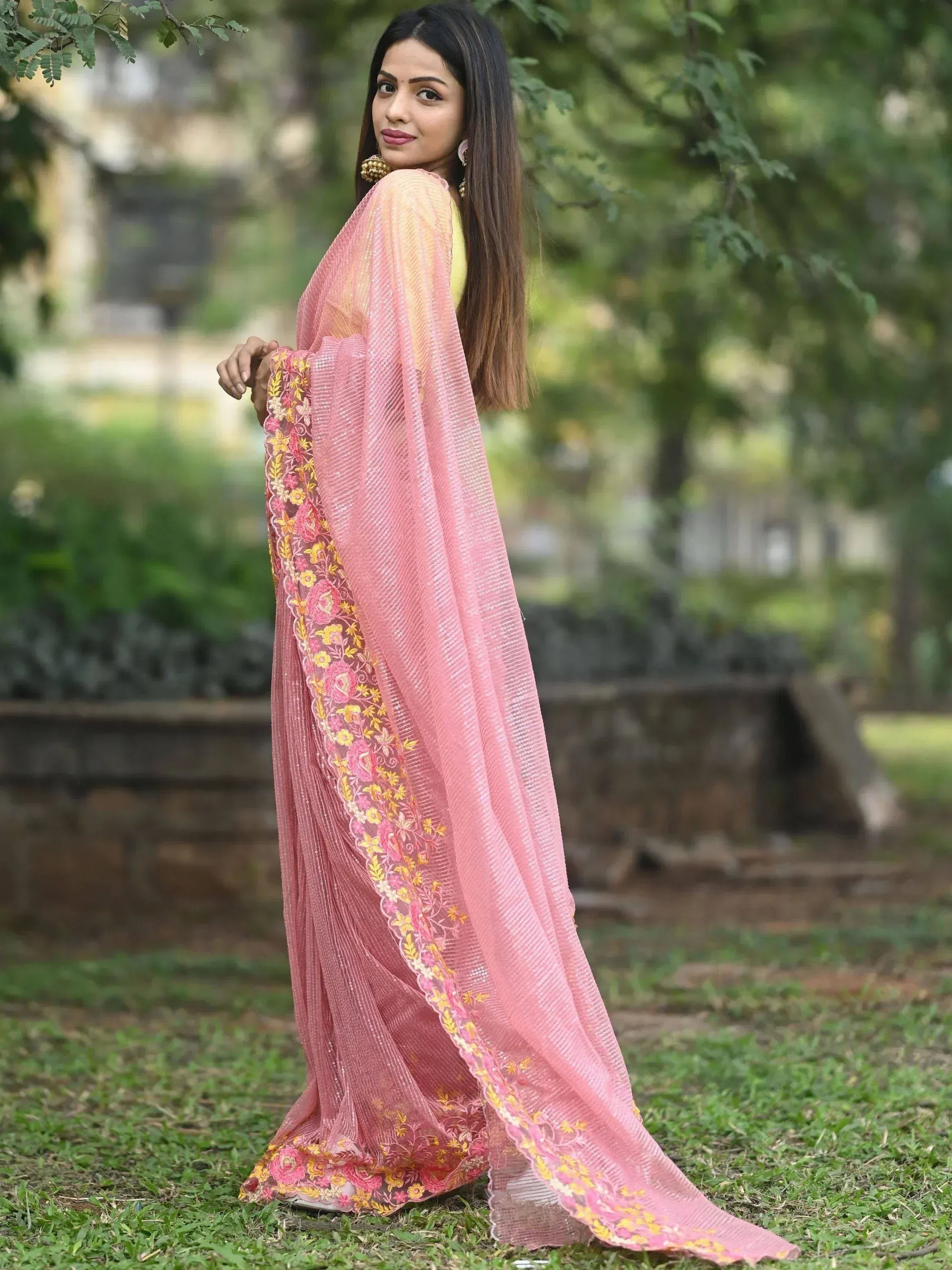 Woman in pink floral embroidered saree with yellow blouse, outdoor garden setting