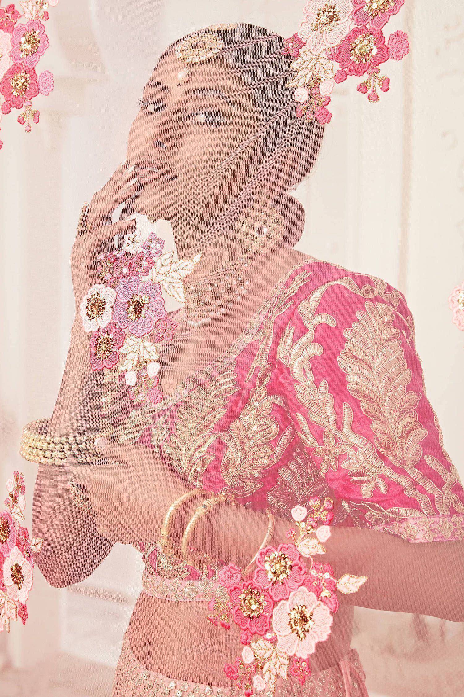 Pink embroidered lehenga choli with floral appliqués, gold jewelry, and sheer veil for Indian weddings