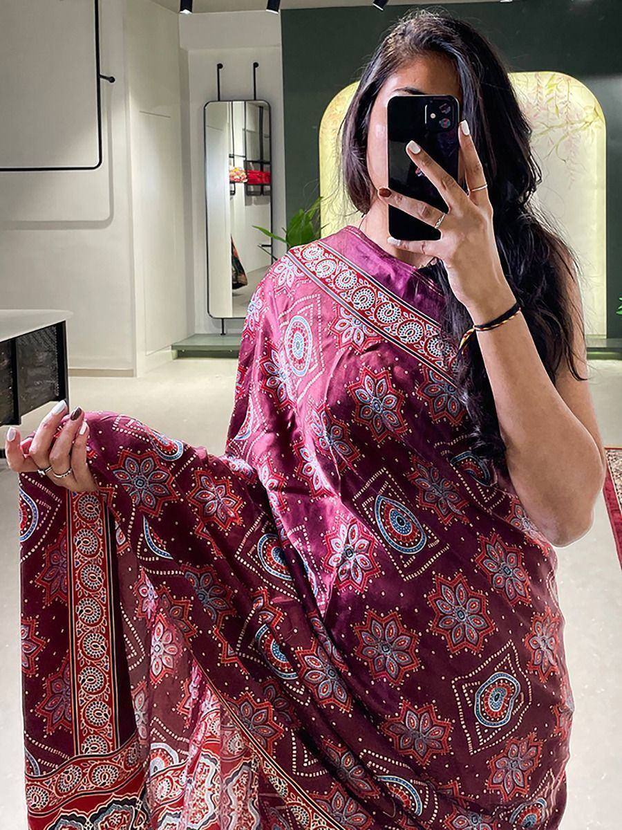 Woman in maroon printed saree with floral motifs, taking mirror selfie in boutique