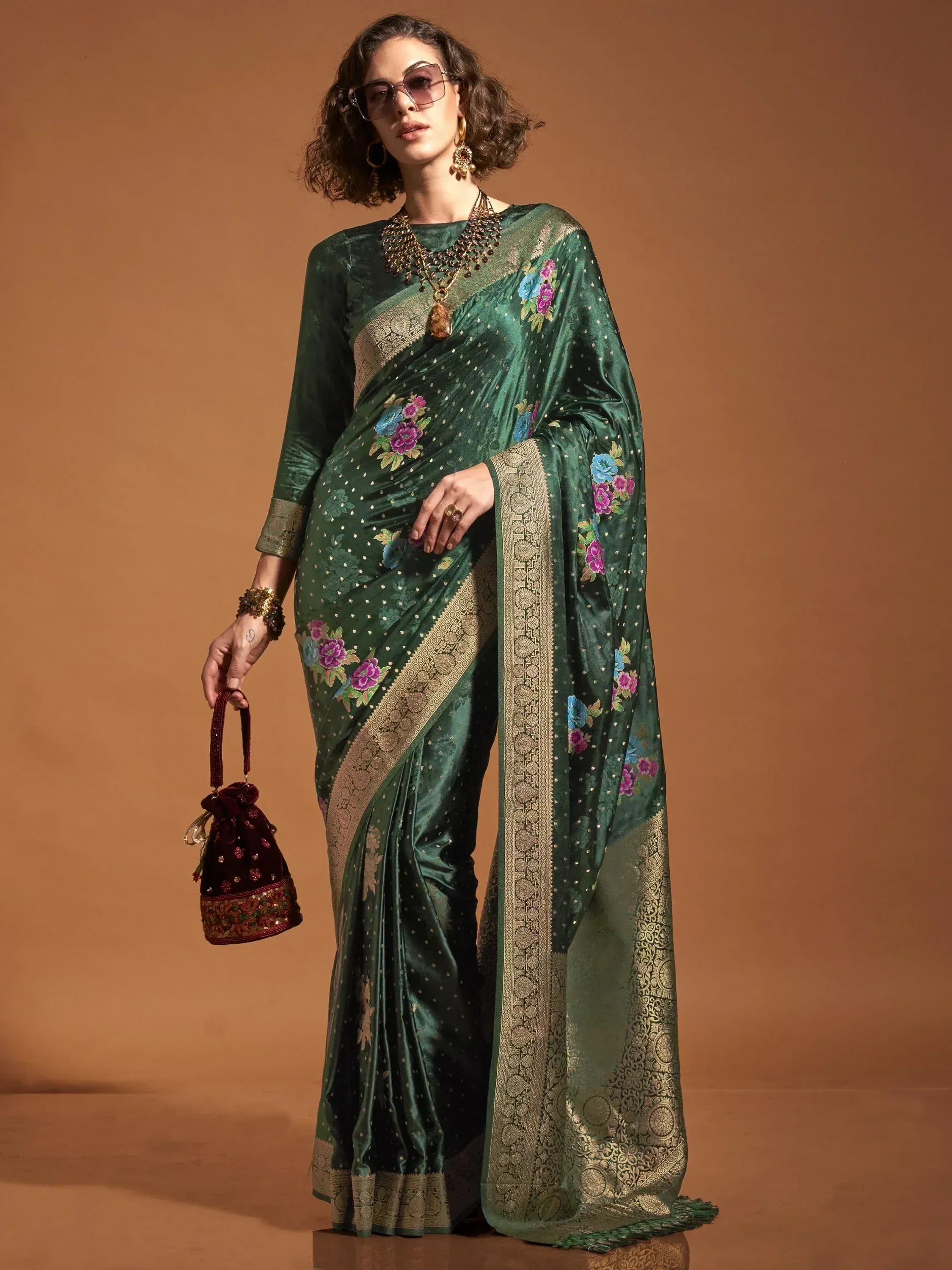 Emerald green velvet saree with floral embroidery and gold border, paired with matching blouse and potli bag