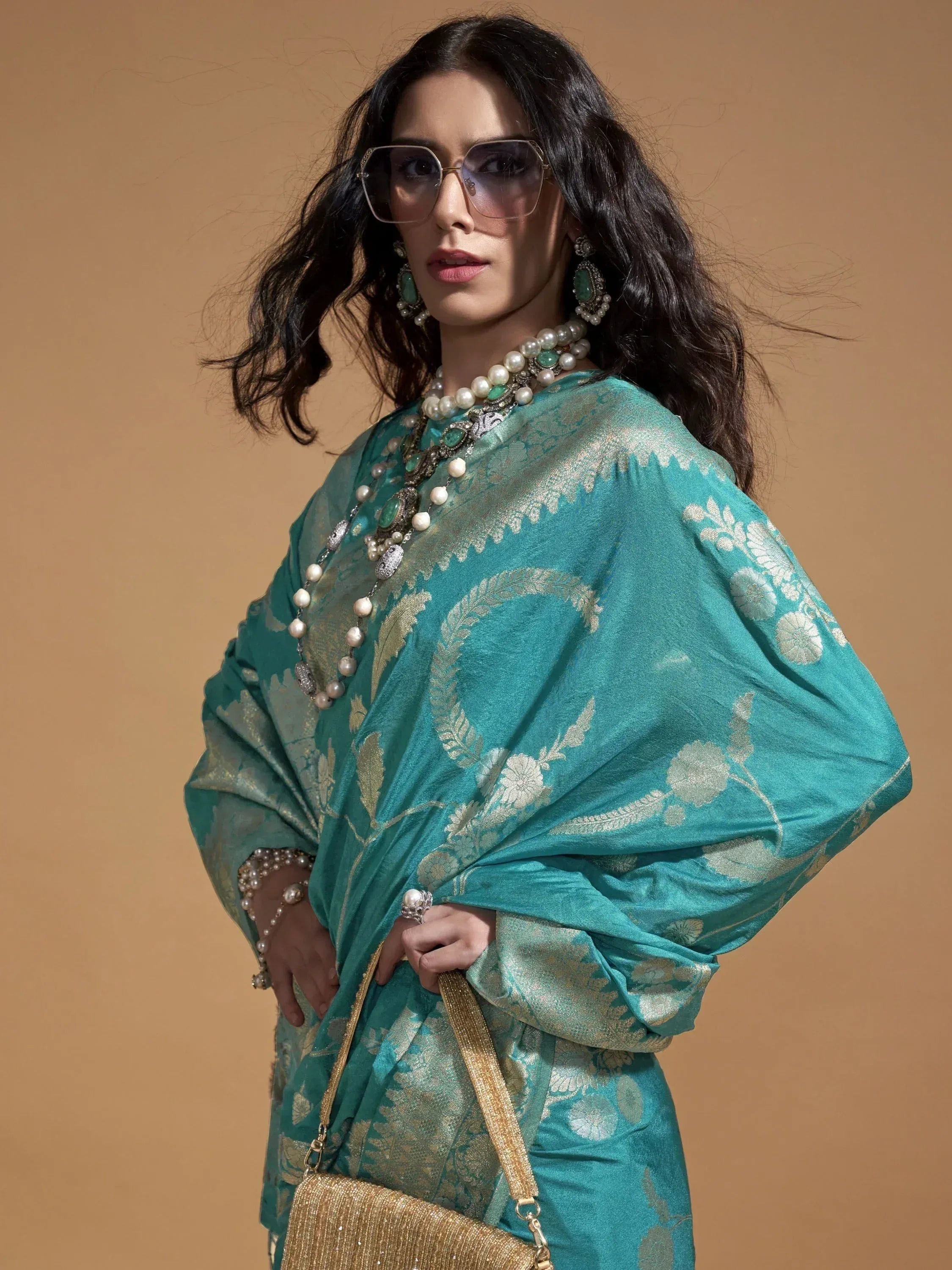 Teal ethnic gown with gold floral embroidery, pearl jewelry, and sunglasses for festive occasions