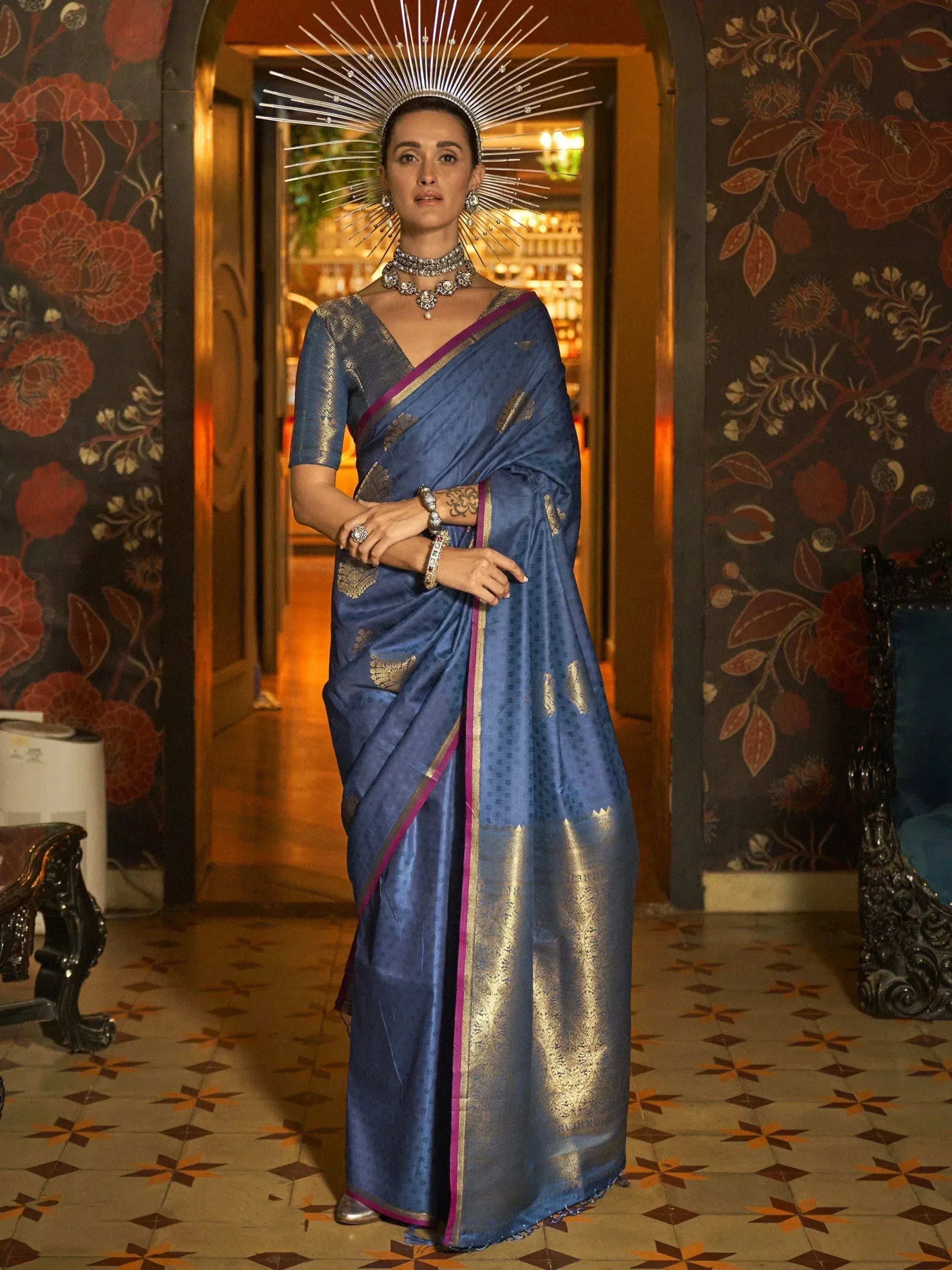 Elegant blue silk saree with gold zari and purple border, paired with statement jewelry and a radiant crown.