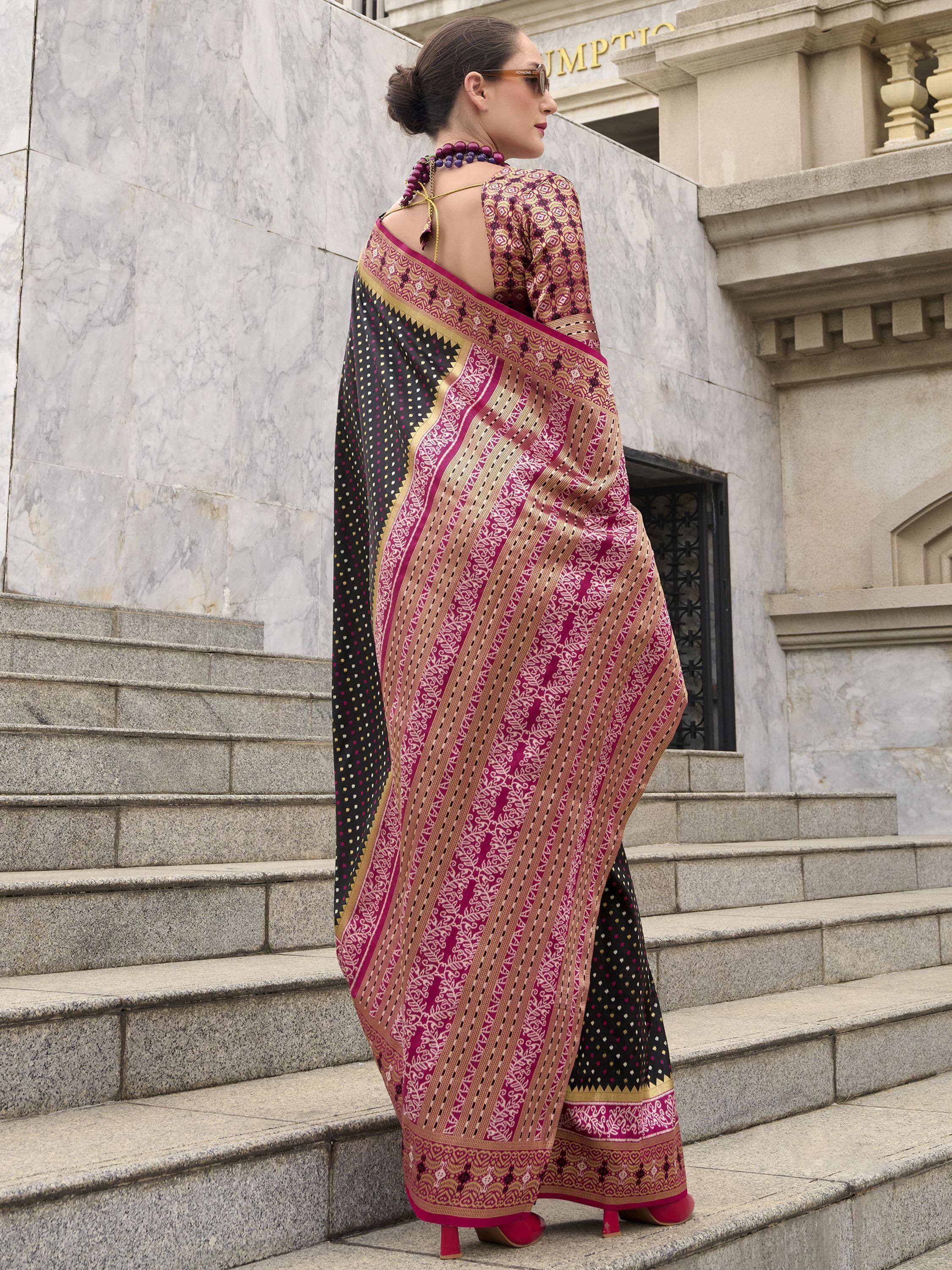 Woman in elegant maroon and black printed saree with gold border, standing on stone steps