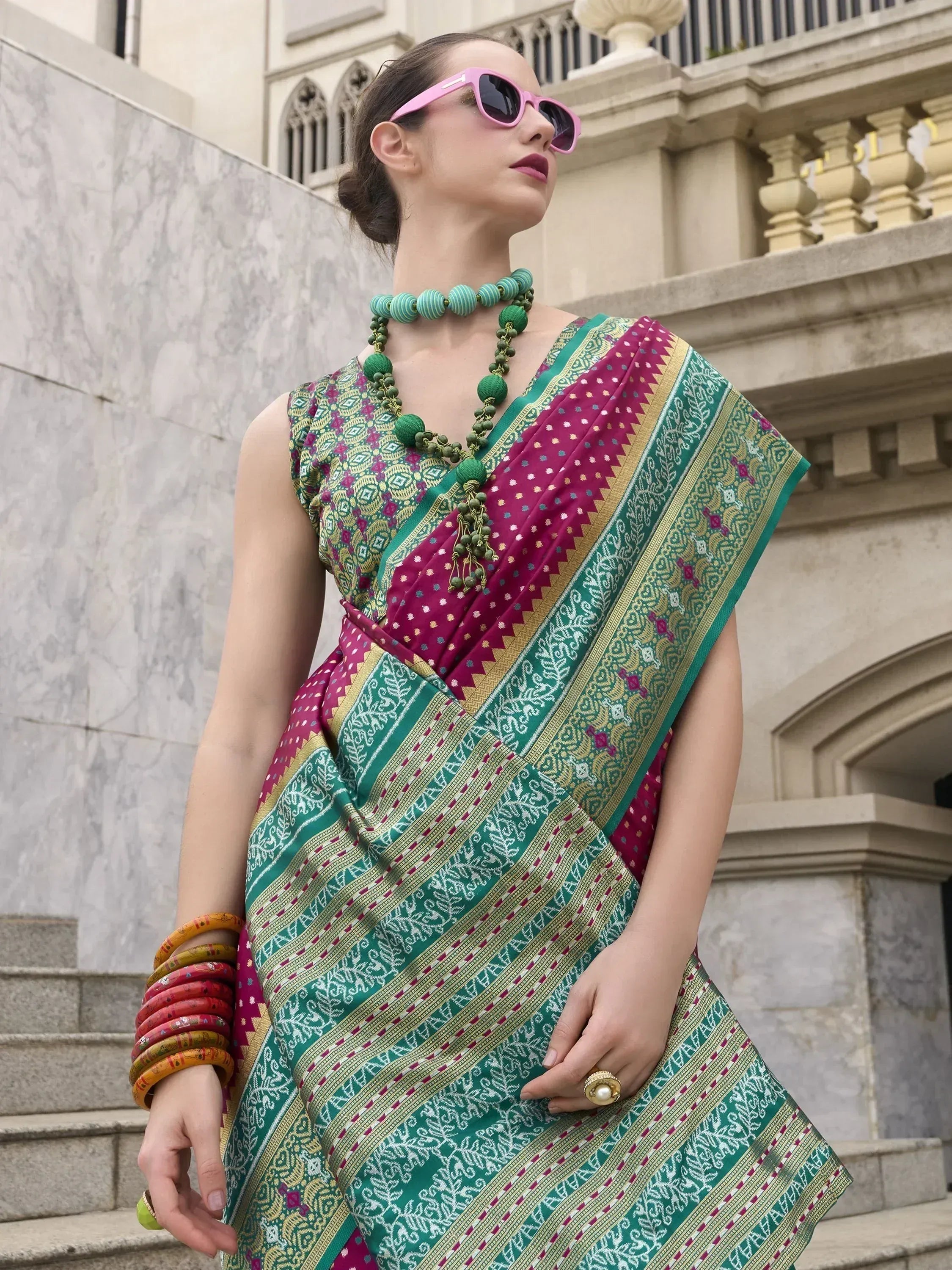 Woman in vibrant green and pink ethnic saree with intricate patterns, styled with bangles and sunglasses