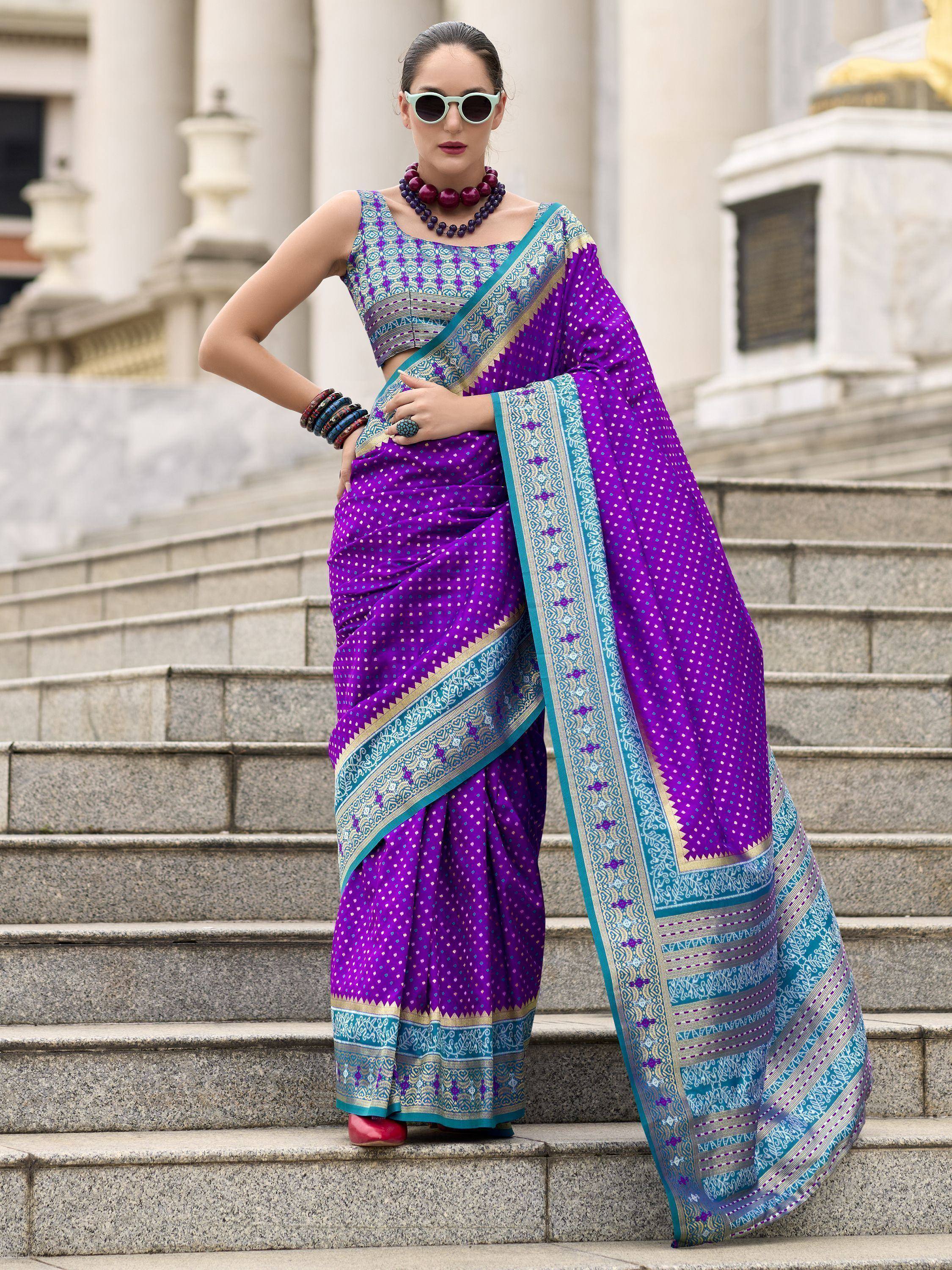 Vibrant purple saree with teal and gold border, paired with patterned blouse, worn on stone steps