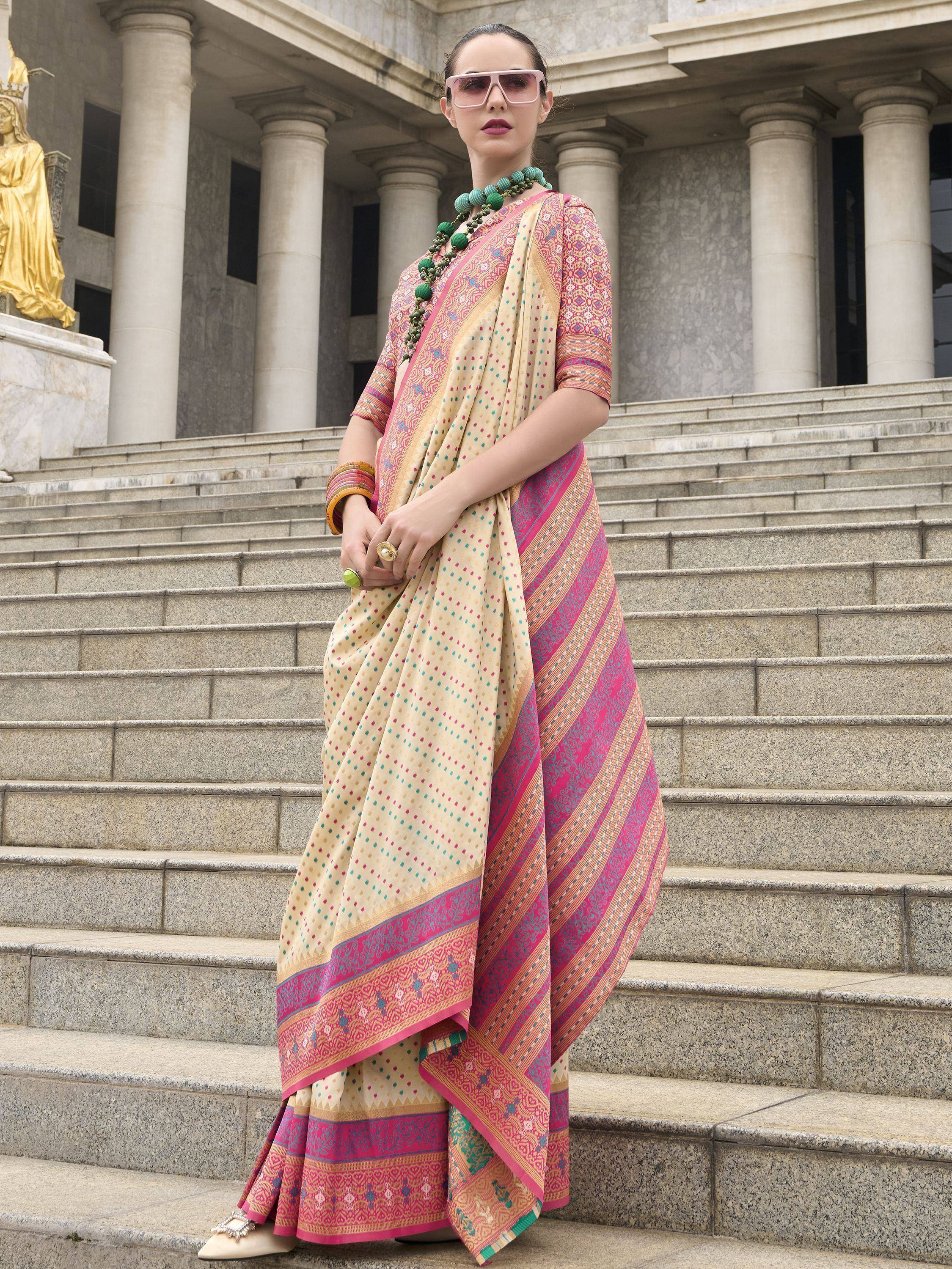 Woman in colorful printed saree with pink border, standing on stone steps near columns