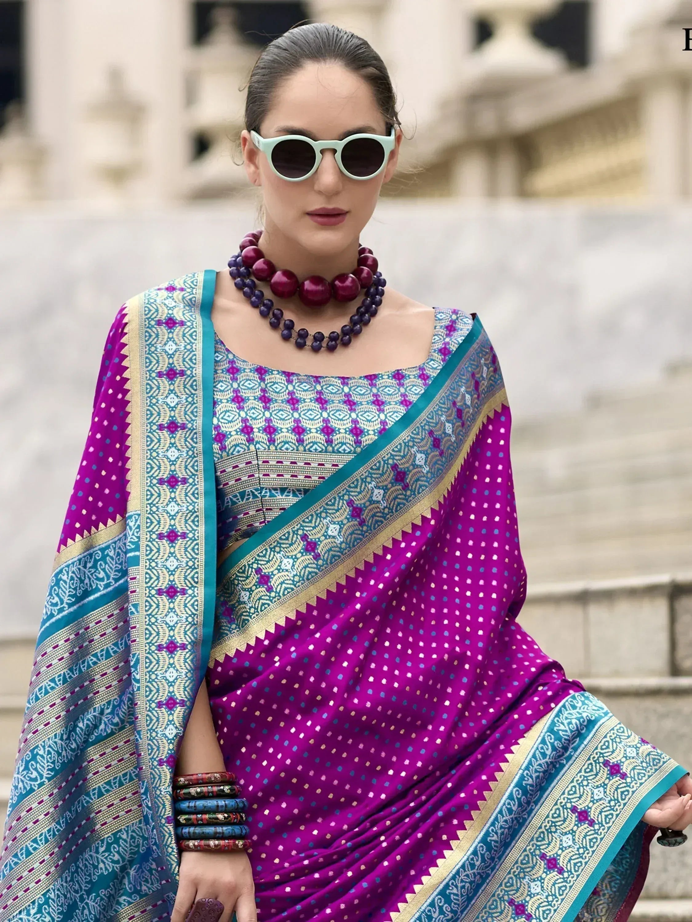 Vibrant purple and teal printed saree with ethnic patterns, styled with statement jewelry and sunglasses