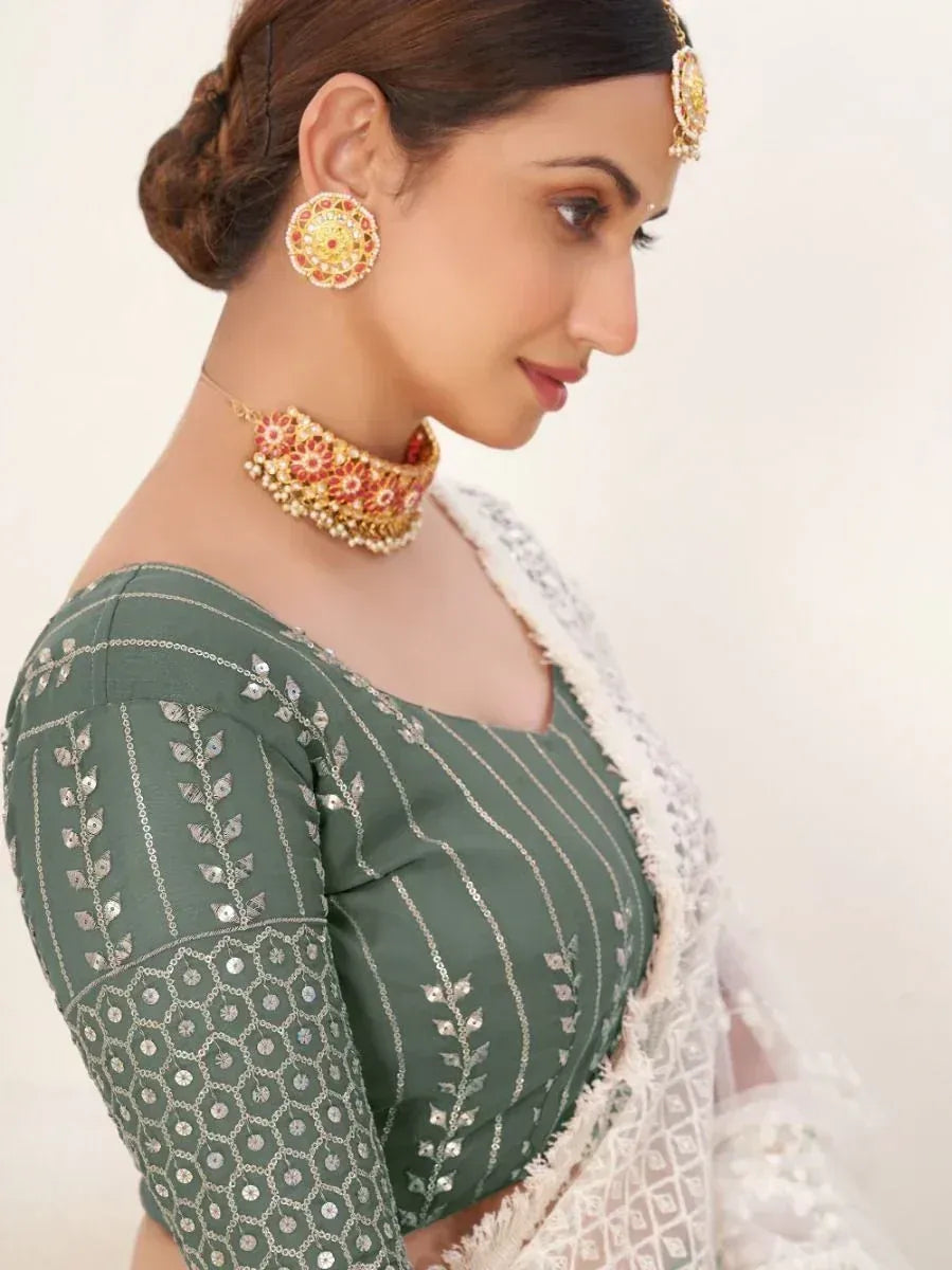 Woman in olive green embroidered blouse with white saree, traditional Indian jewelry
