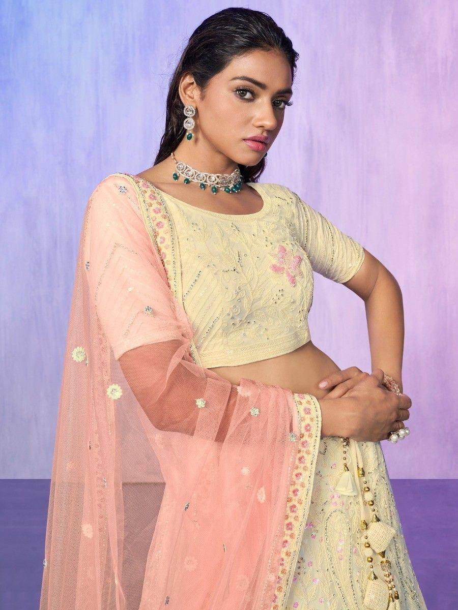 Elegant cream lehenga choli with pink dupatta, floral embroidery, and green jewelry for Indian ethnic wear