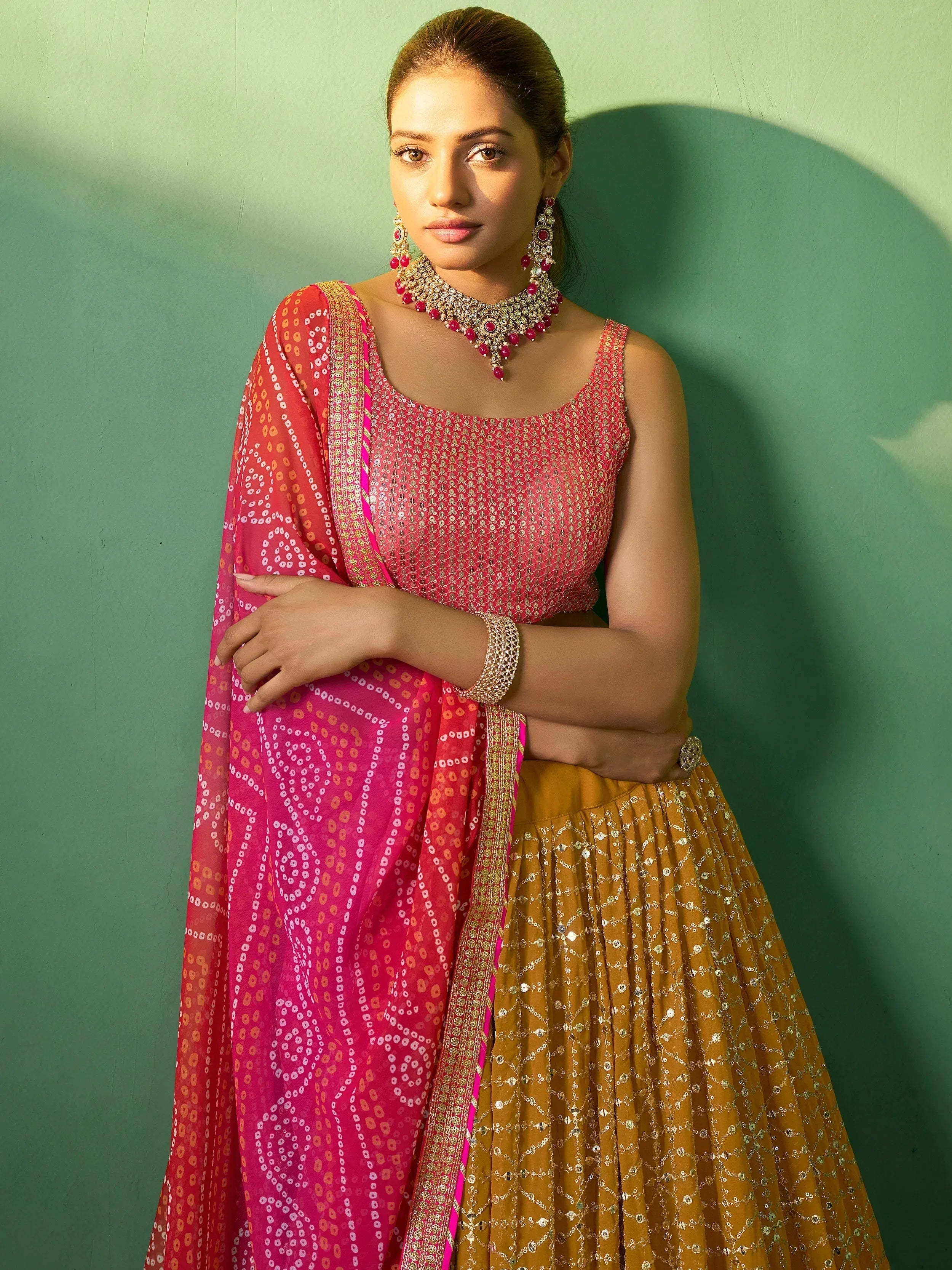Woman in vibrant pink and mustard Indian lehenga choli with embroidery, paired with traditional jewelry