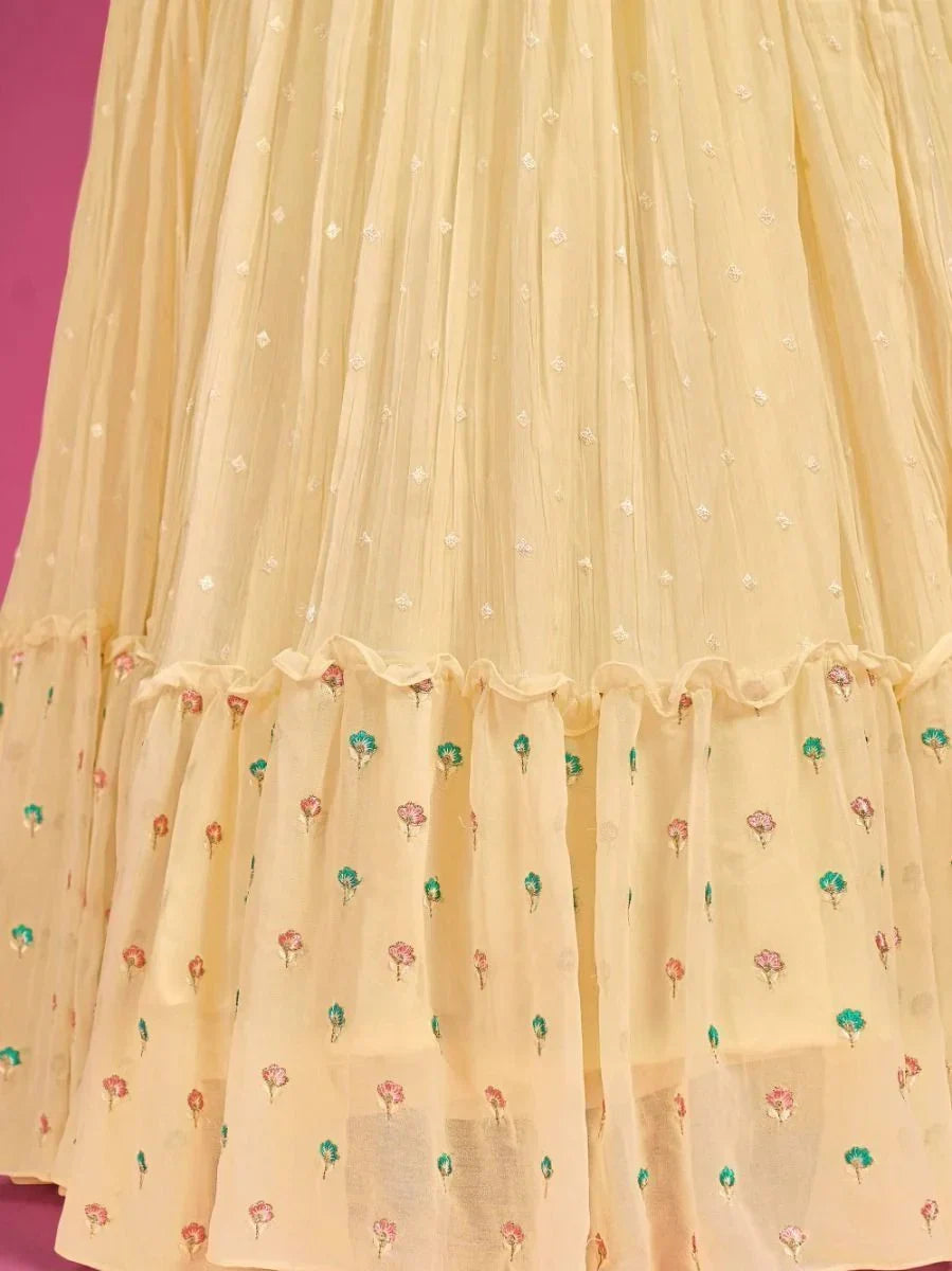 Yellow embroidered lehenga with floral patterns and ruffled hem on a pink background