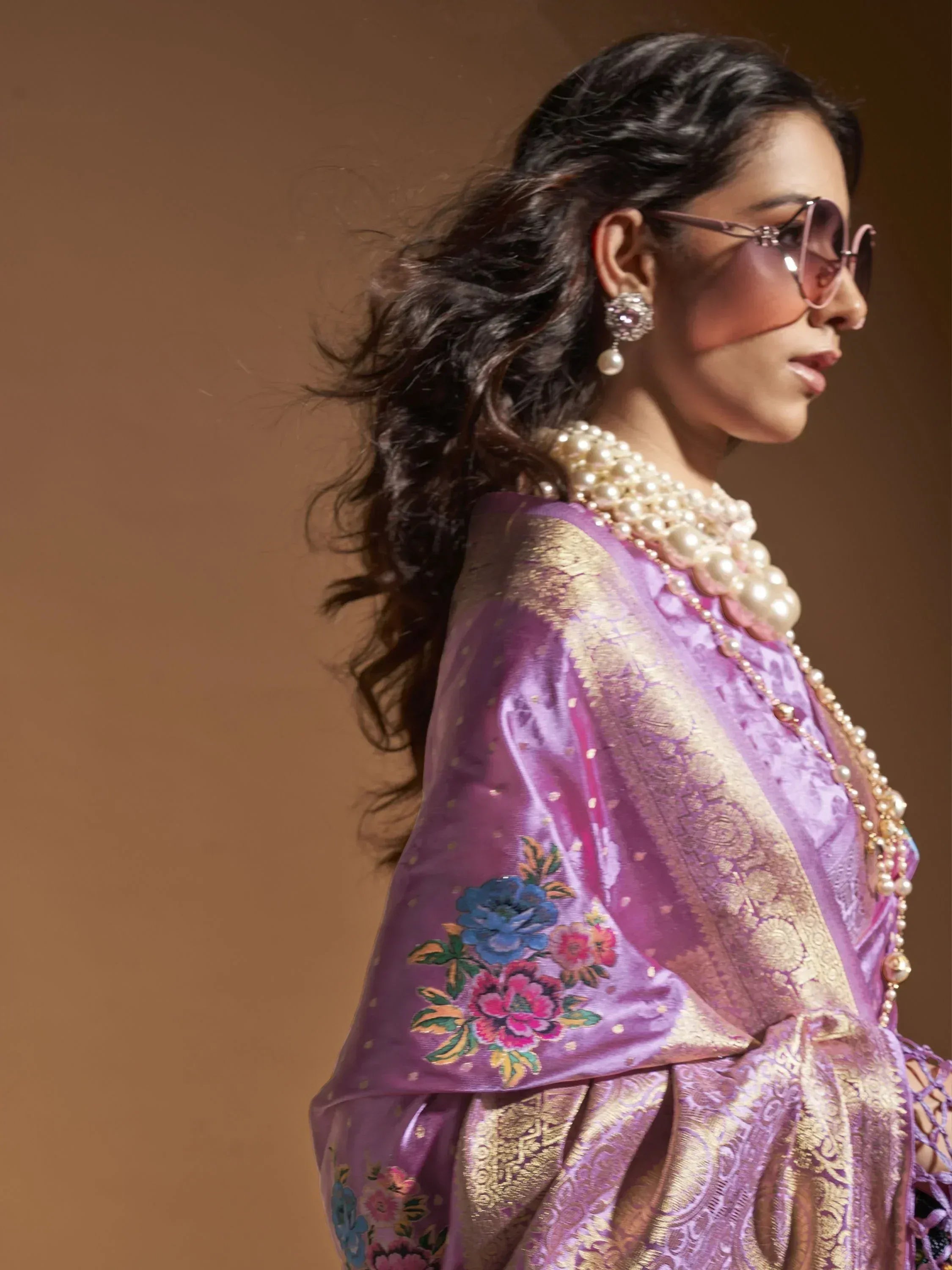 Purple and gold ethnic gown with floral embroidery, styled with pearl jewelry and sunglasses
