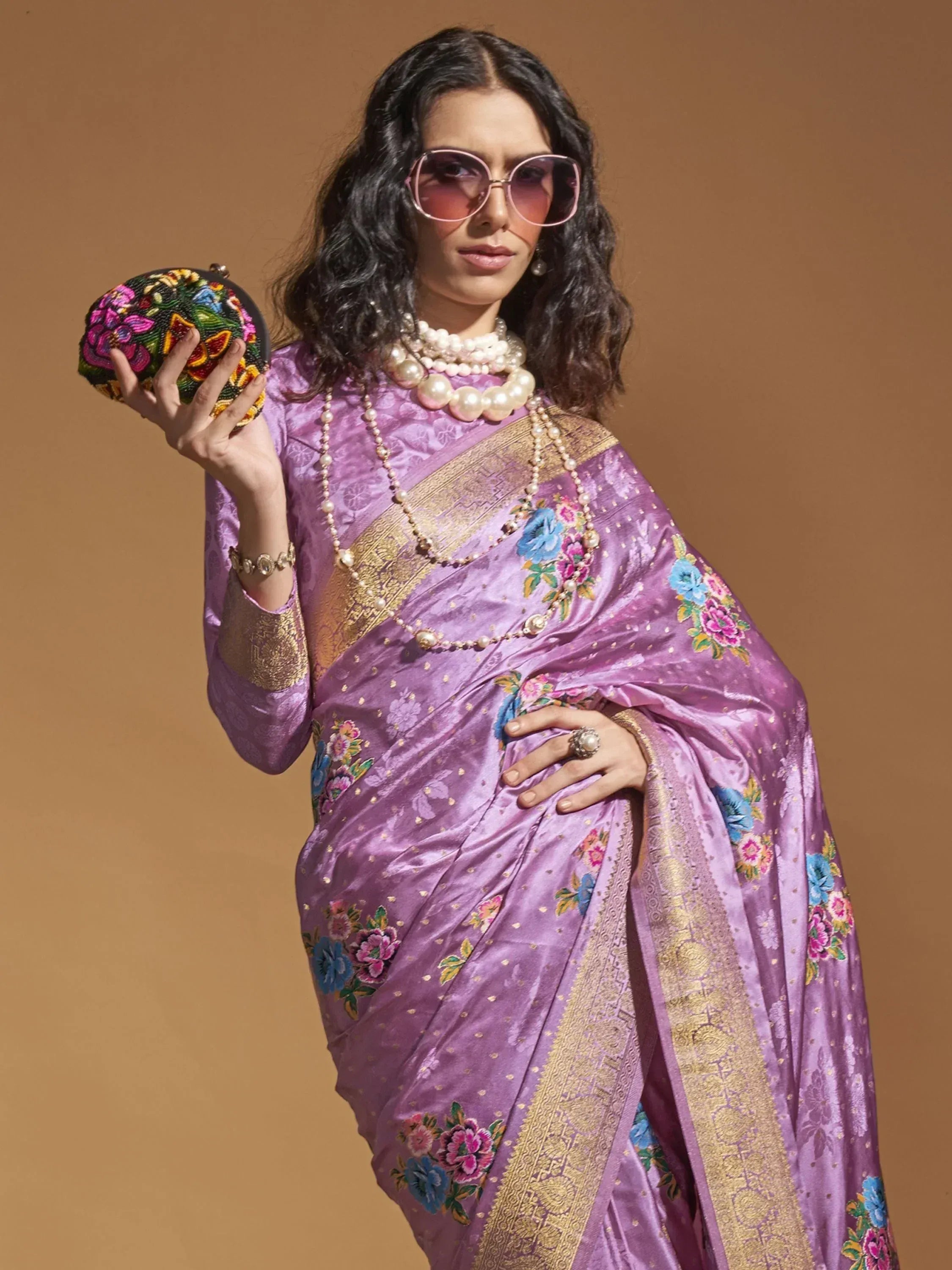 Purple floral saree with gold border, pearl jewelry, and beaded clutch for ethnic wear