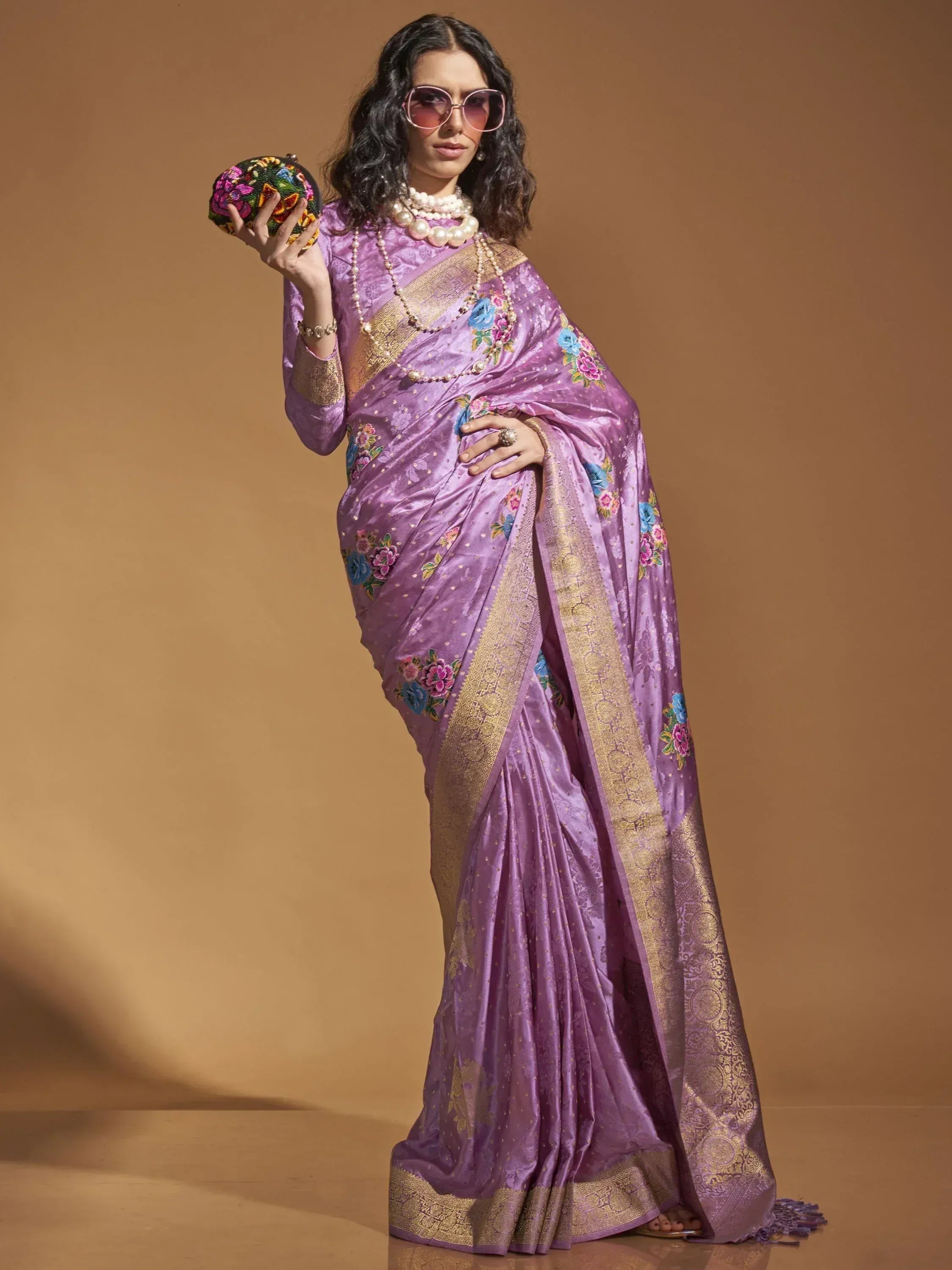 Purple floral embroidered saree with gold border, styled with pearl jewelry and embroidered clutch for Indian ethnic wear
