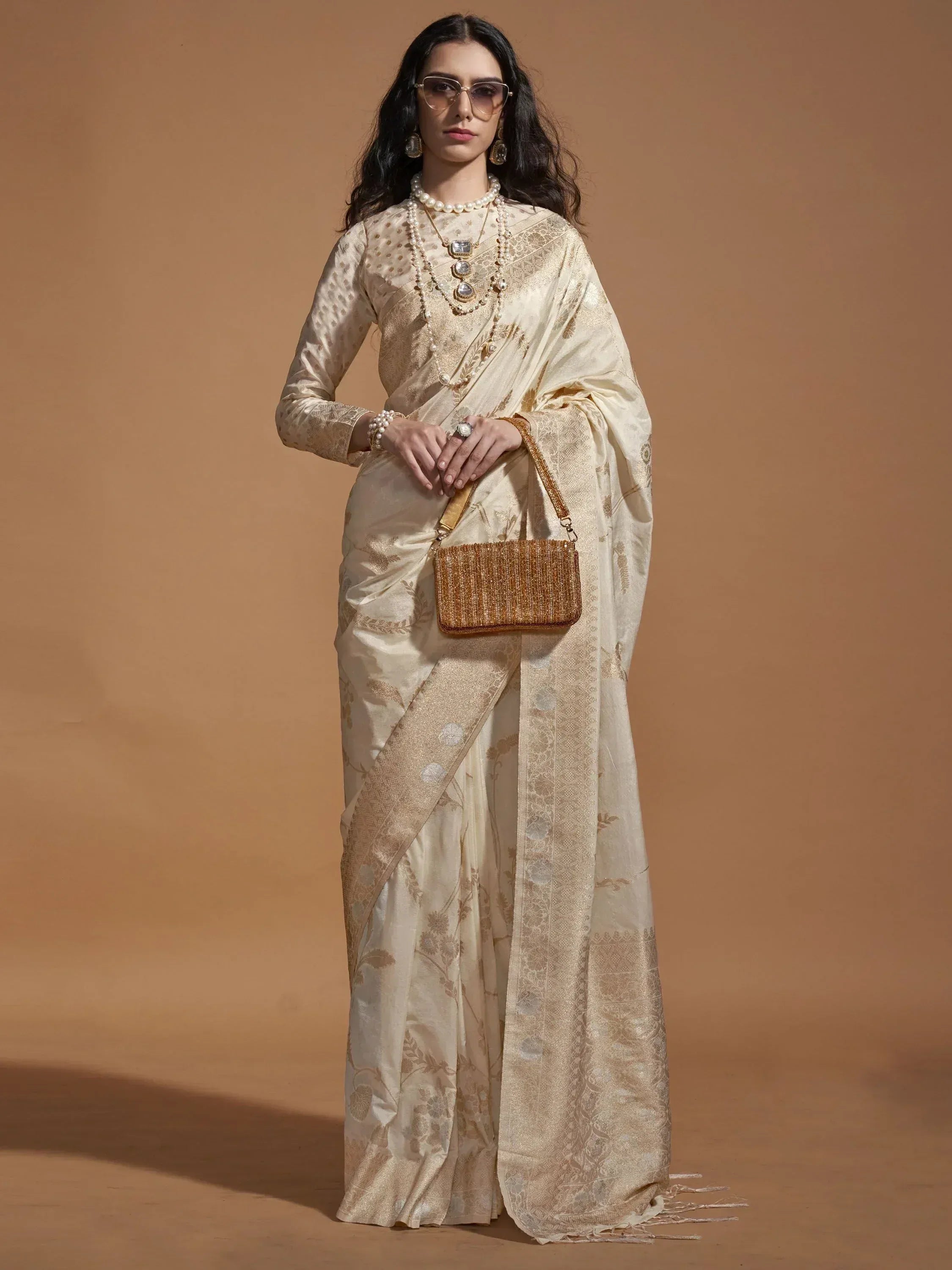 Elegant cream saree with gold floral embroidery, paired with pearl jewelry and a beaded clutch for Indian ethnic wear.