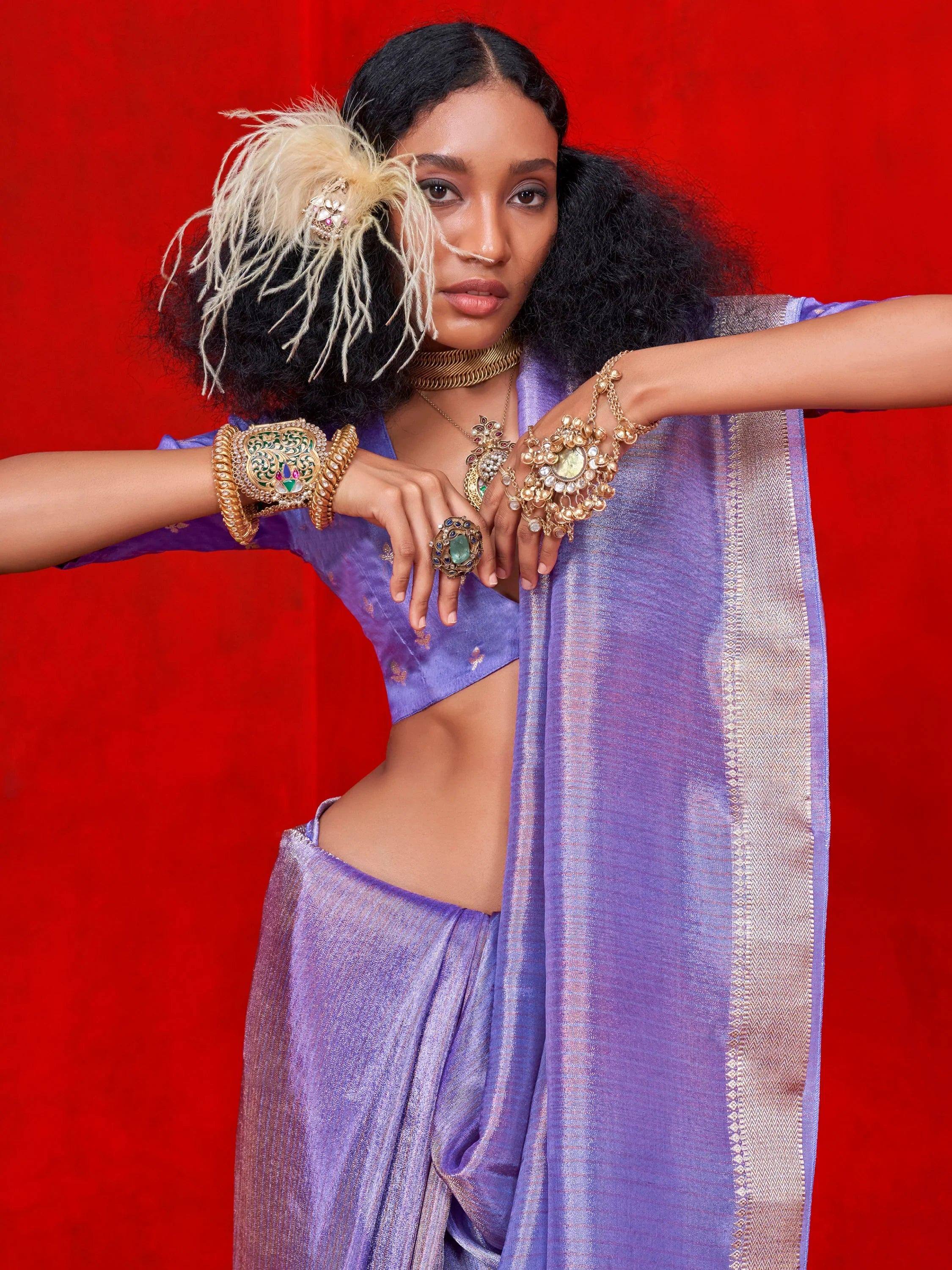 Purple ethnic saree with gold jewelry and feather hair accessory against red background