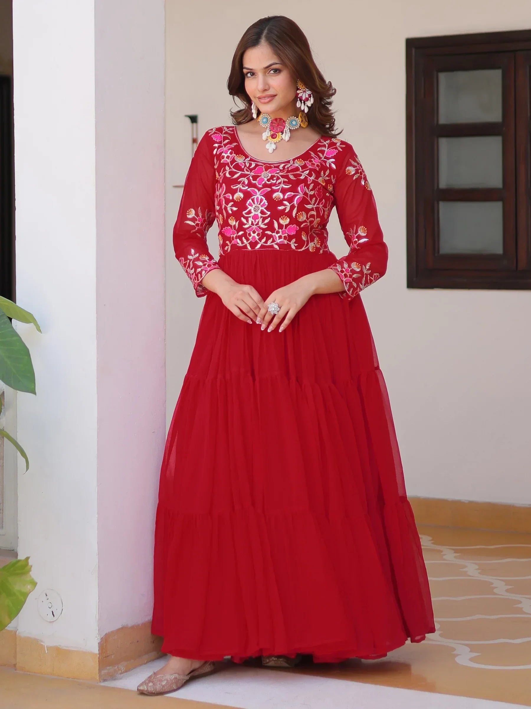 Woman wearing red embroidered ethnic gown with floral jewelry, standing outdoors