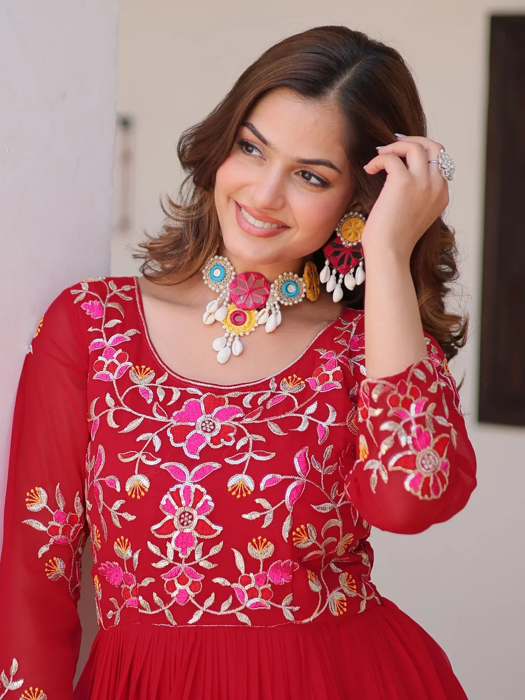 Red embroidered ethnic gown with floral design, paired with colorful statement jewelry for festive occasions
