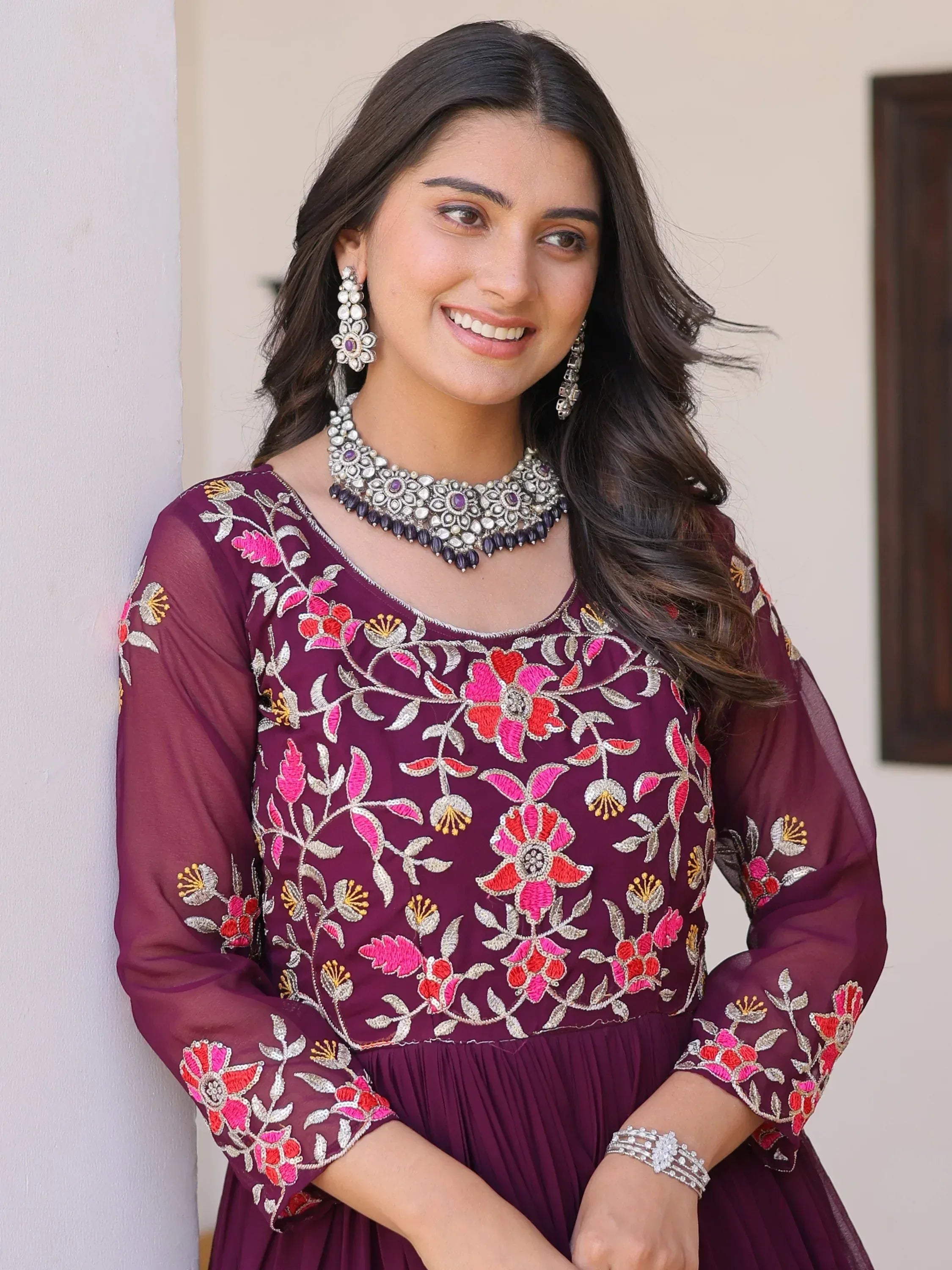 Woman in maroon floral embroidered ethnic gown with statement jewelry, perfect for Indian occasions.