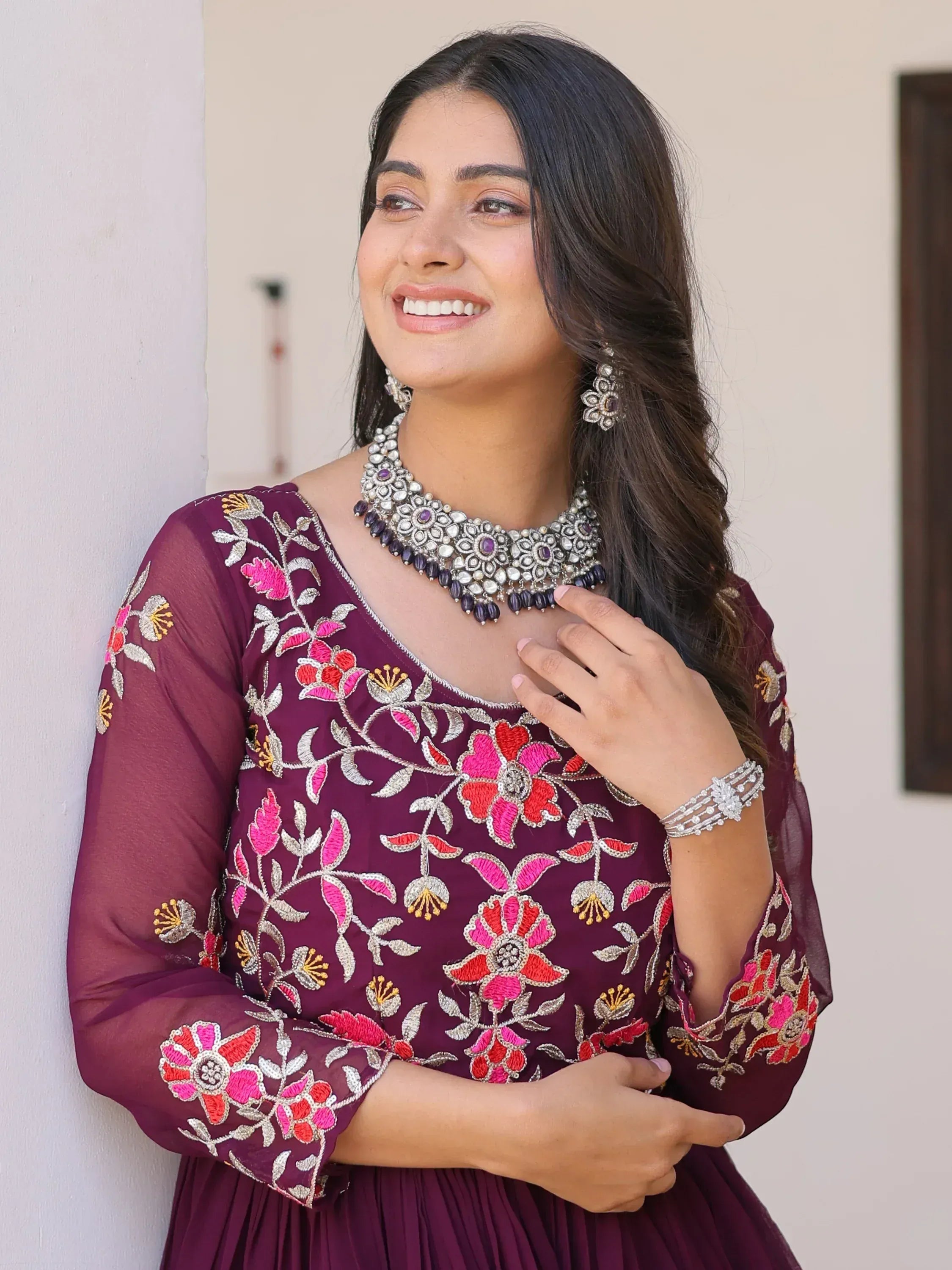 Woman in maroon floral embroidered ethnic gown with traditional jewelry, perfect for Indian festive occasions.
