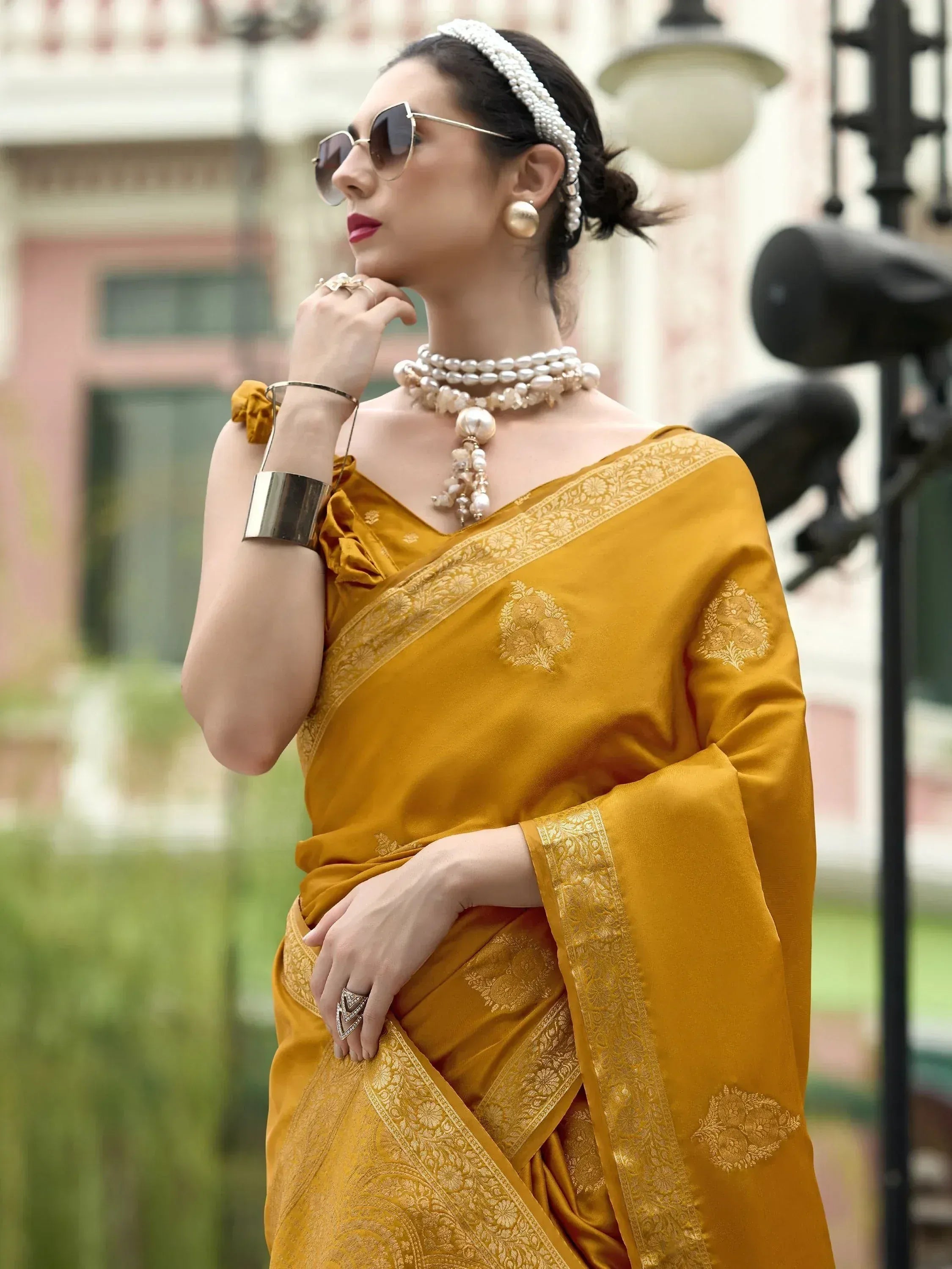 Elegant woman in mustard yellow designer saree with gold embroidery, pearl jewelry, and sunglasses