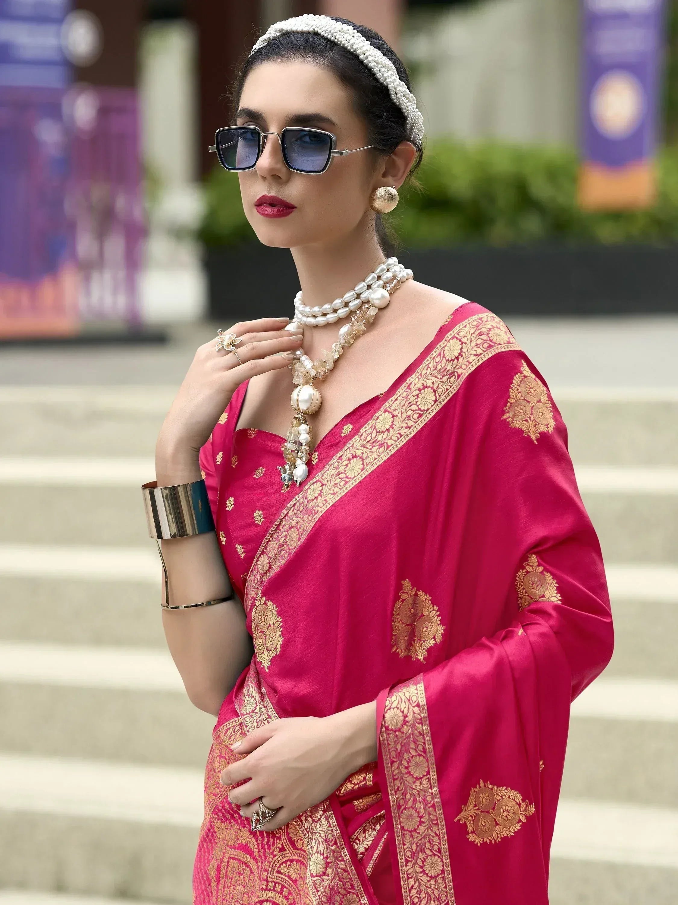 Woman in pink designer saree with gold embroidery, pearl jewelry, and sunglasses for ethnic wear