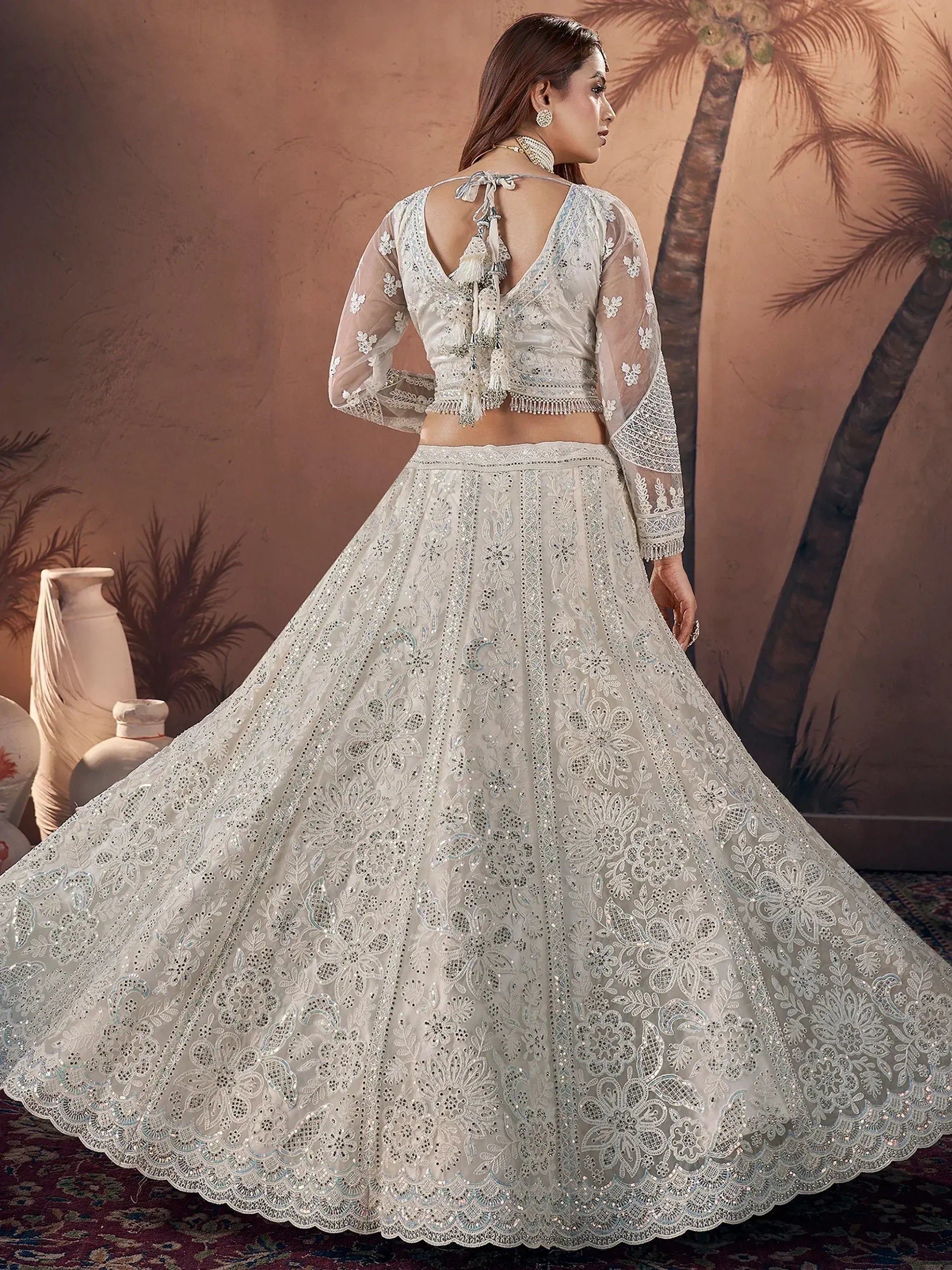 Elegant white embroidered lehenga choli with sheer sleeves and floral detailing, perfect for Indian weddings or festive occasions.