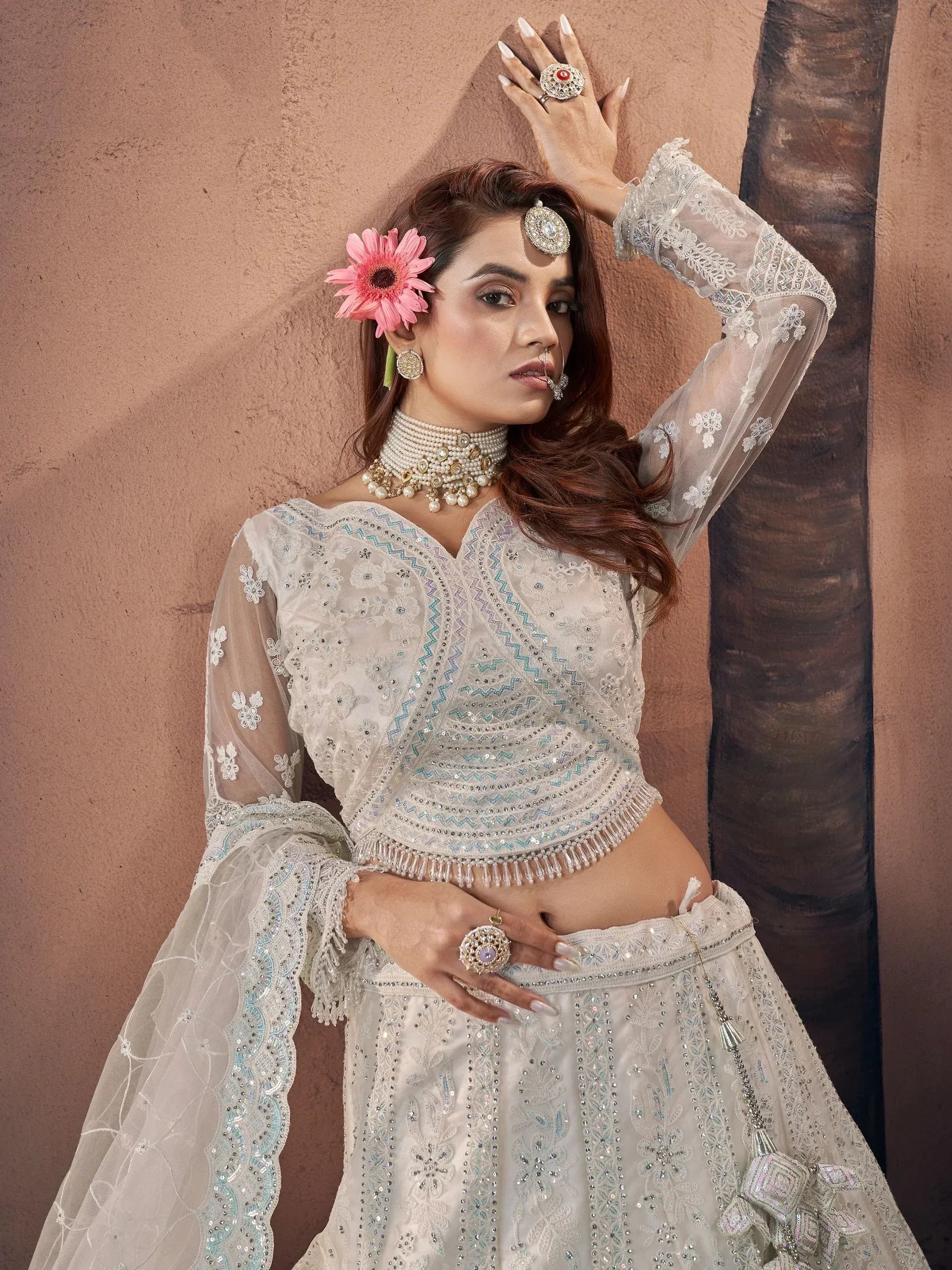 Elegant white embroidered lehenga choli with sheer sleeves, pearl jewelry, and floral hair accessory for Indian ethnic wear.