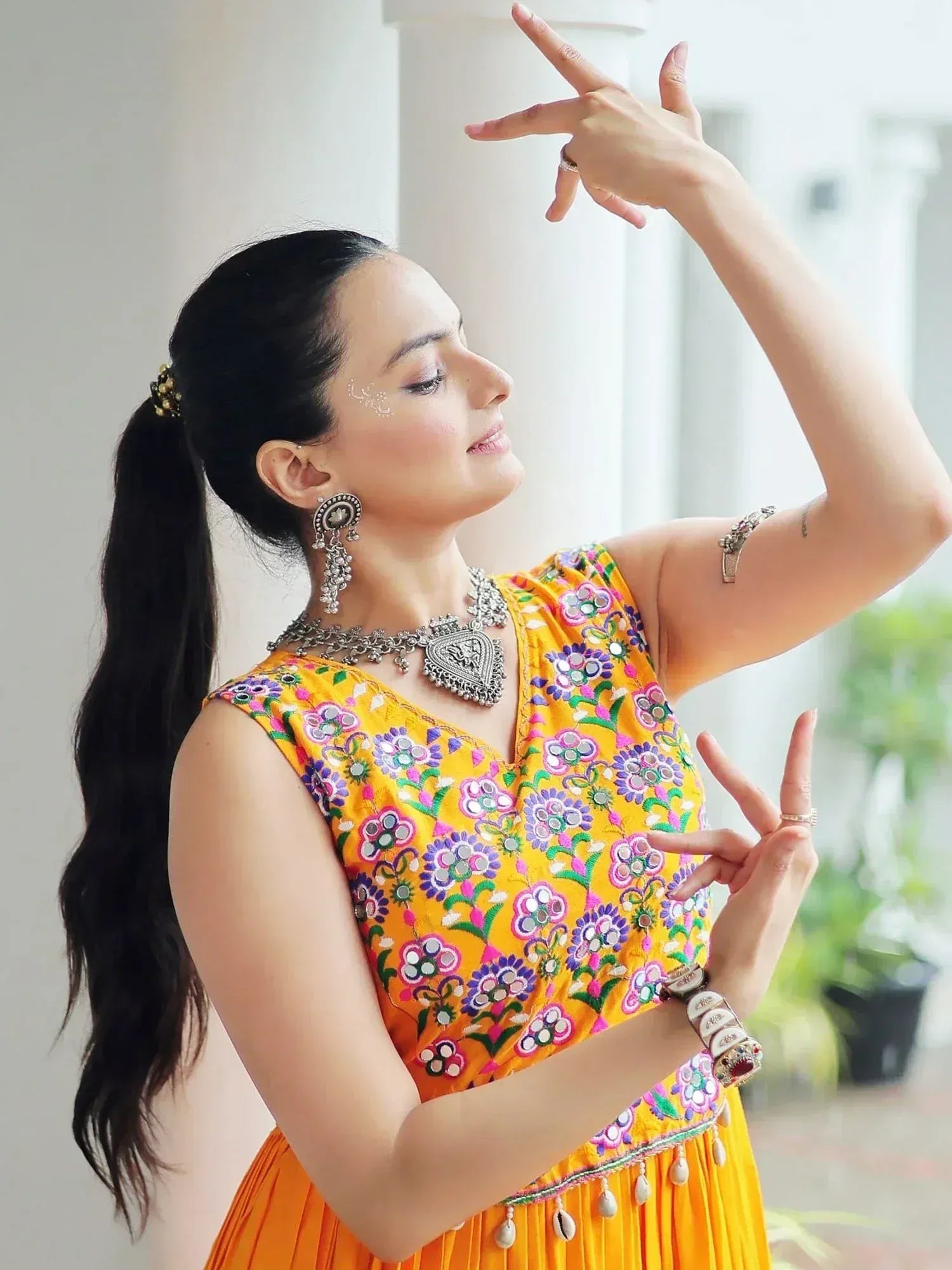 Woman in vibrant yellow floral embroidered ethnic gown with mirror work, styled with traditional jewelry for festive occasions