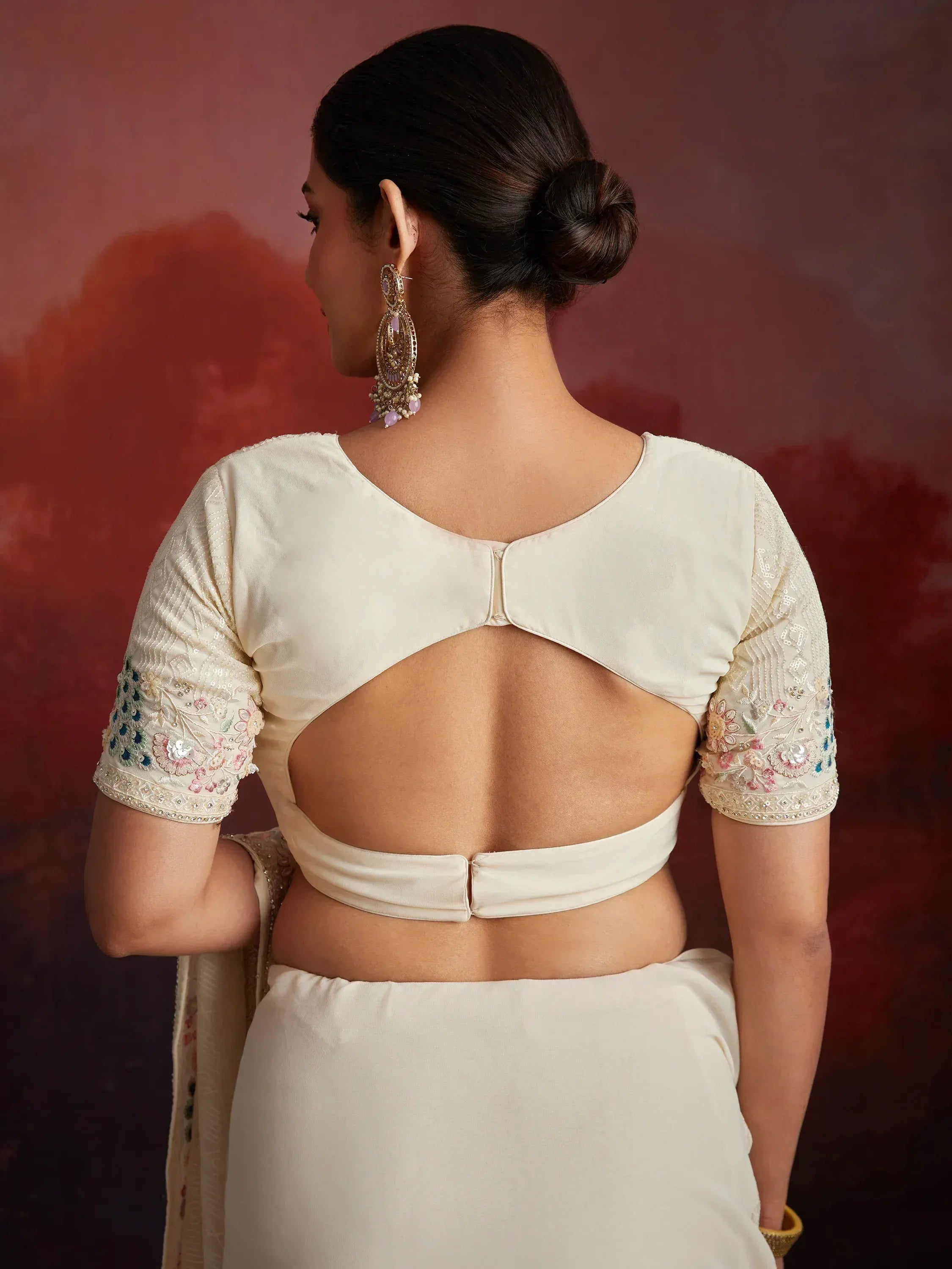 Cream saree blouse with back cutout and floral embroidery, paired with statement earrings