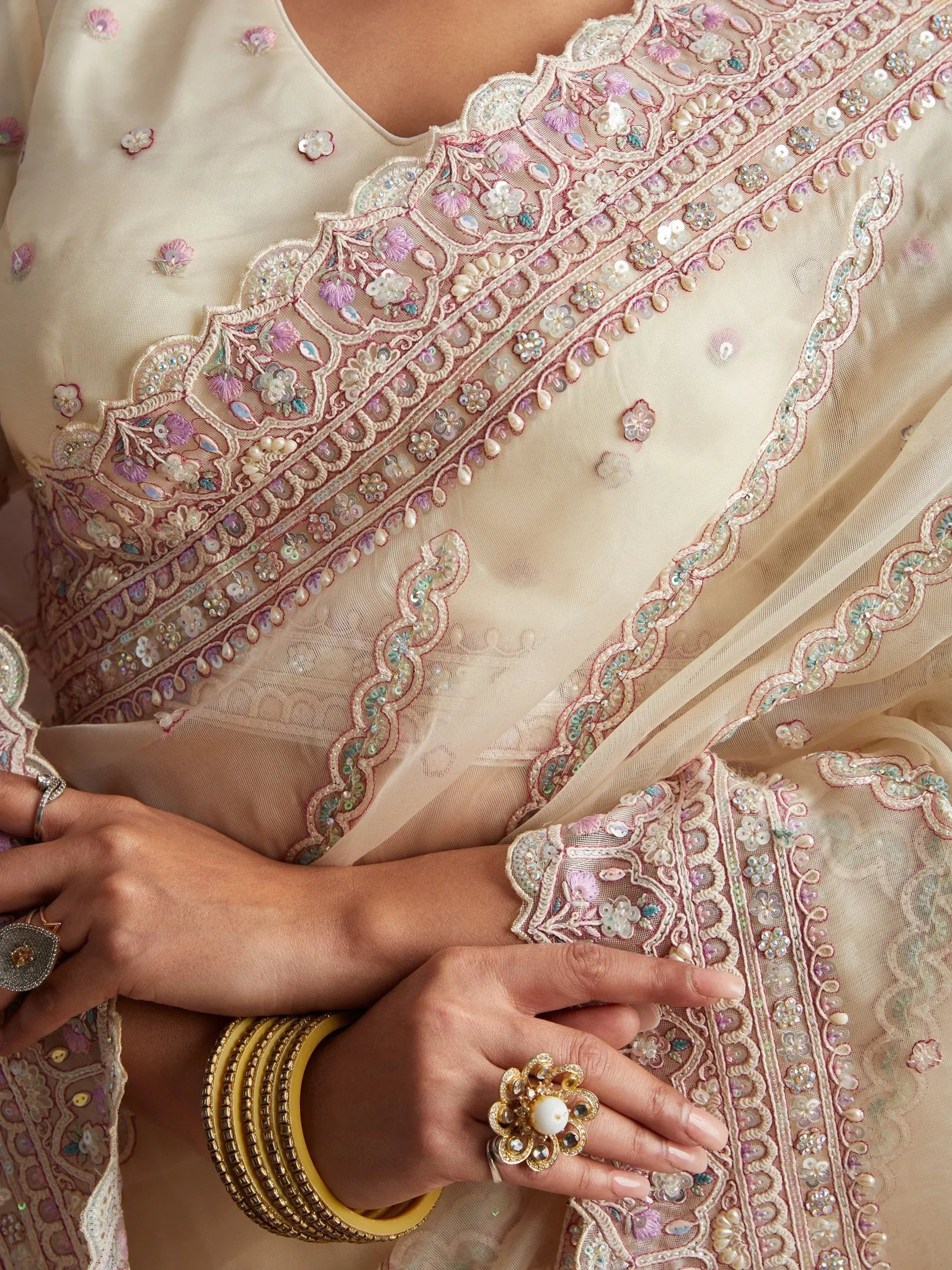 Elegant cream ethnic wear with intricate floral embroidery, sequins, and pearl detailing, paired with traditional bangles and rings.