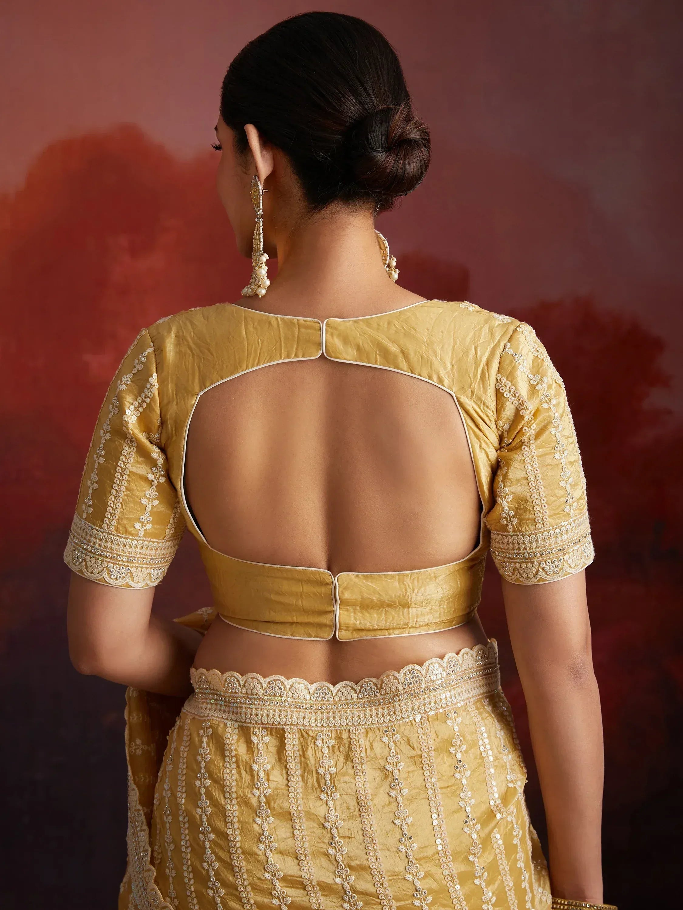 Back view of woman in golden designer lehenga choli with open back and intricate embroidery