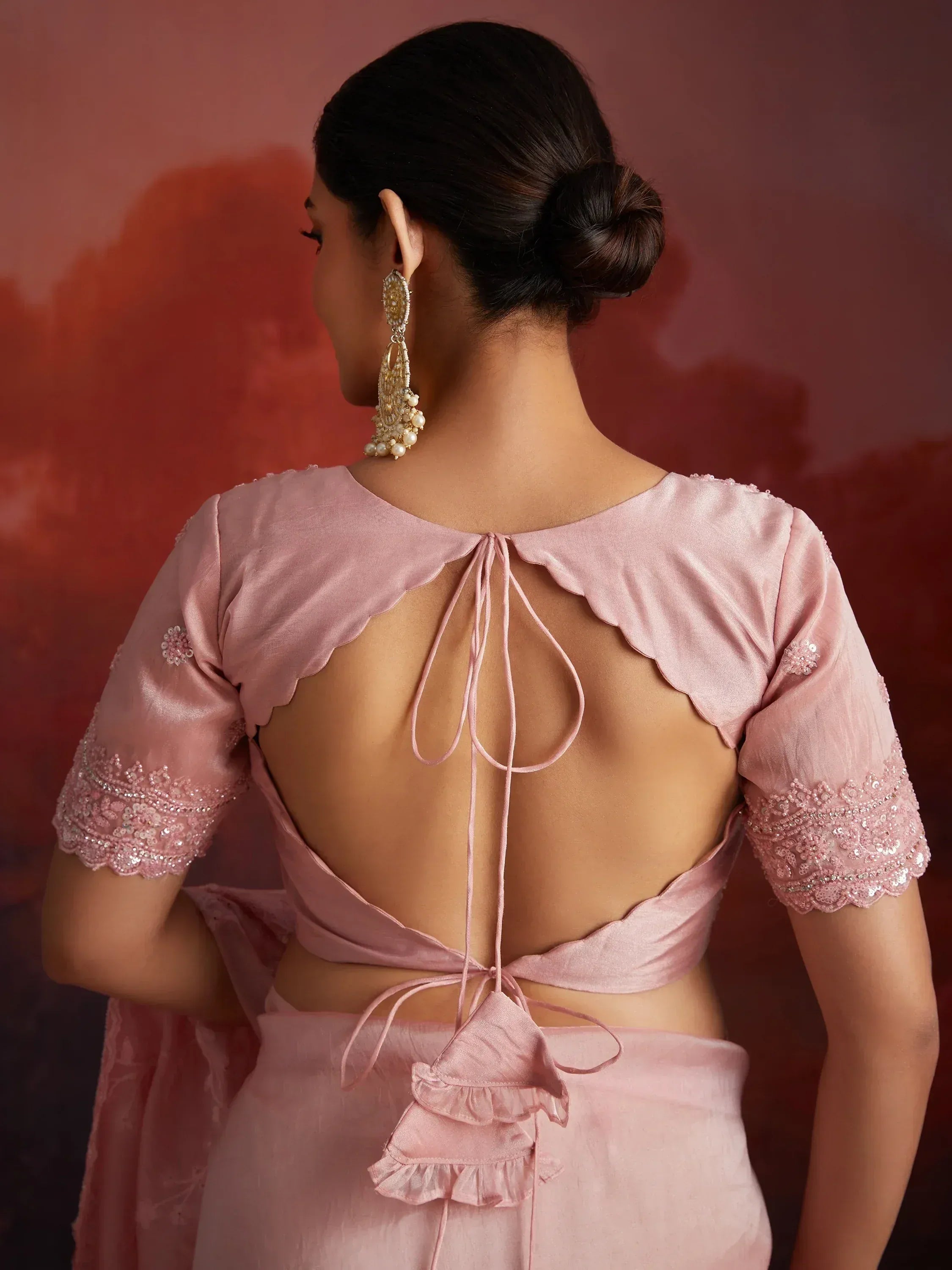 Pink designer lehenga choli with back tie detail, scalloped sleeves, and pearl earrings