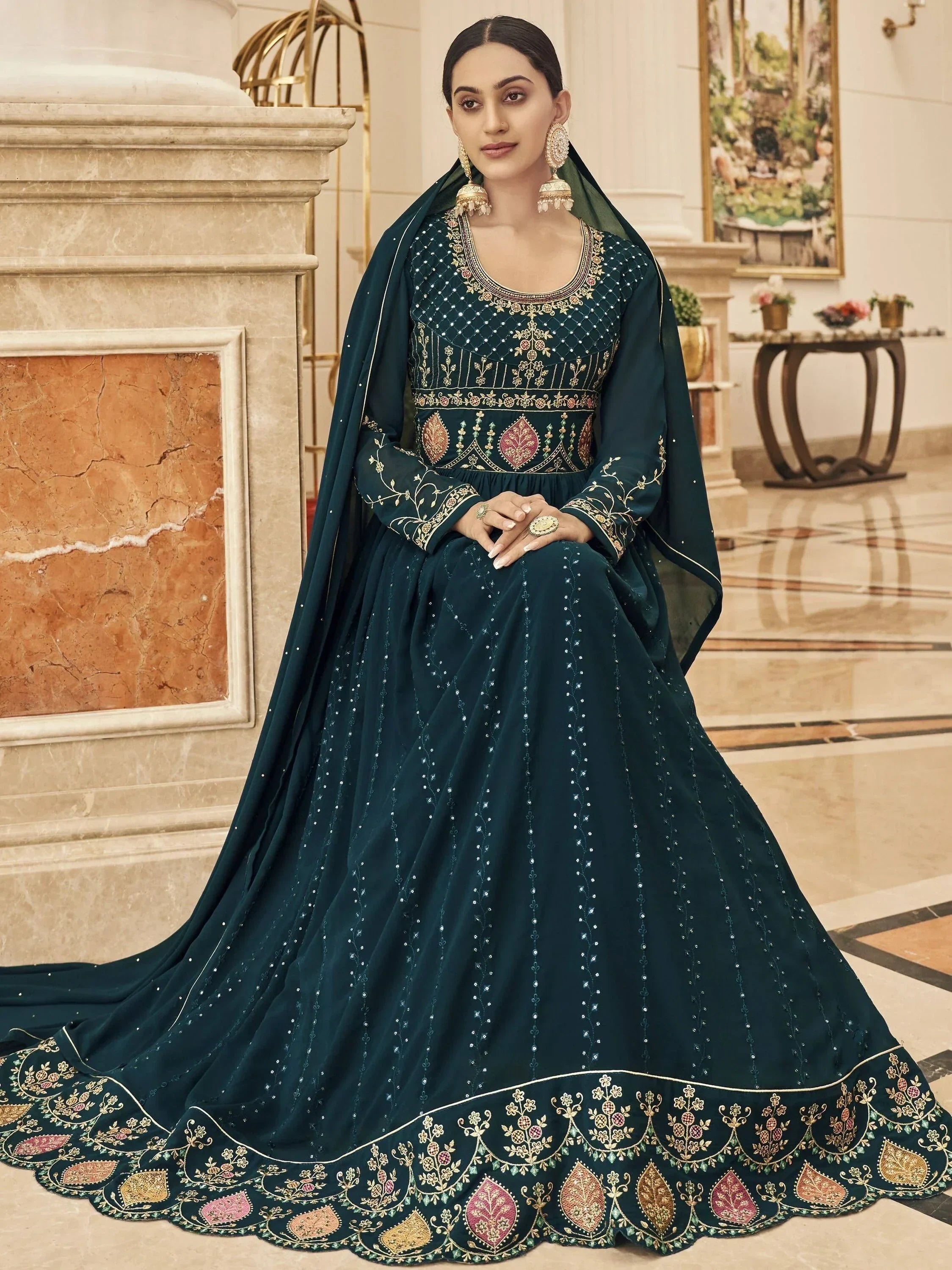 Woman in elegant dark green embroidered Indian ethnic gown with dupatta, sitting indoors