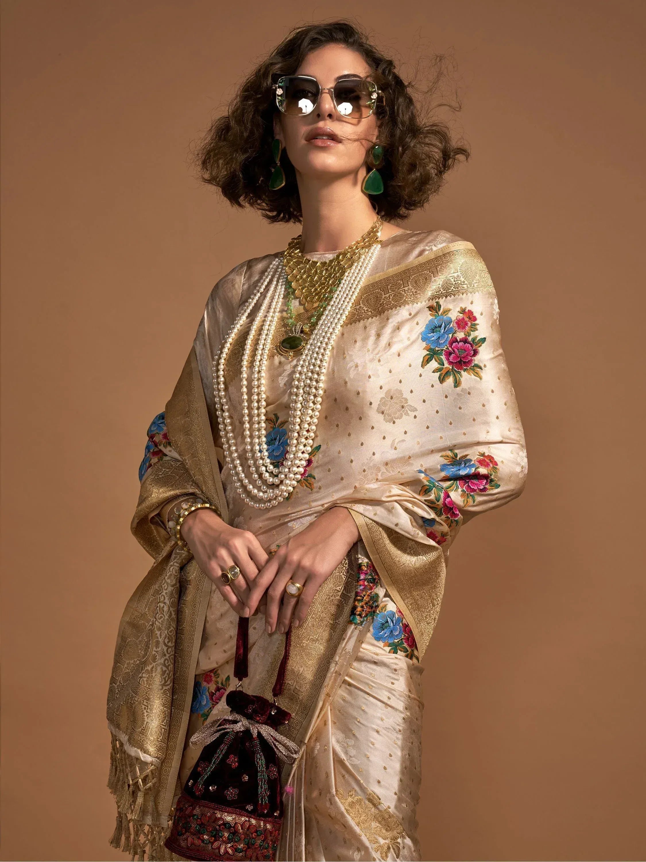 Elegant woman in floral embroidered saree with gold border, pearl necklace, and statement sunglasses