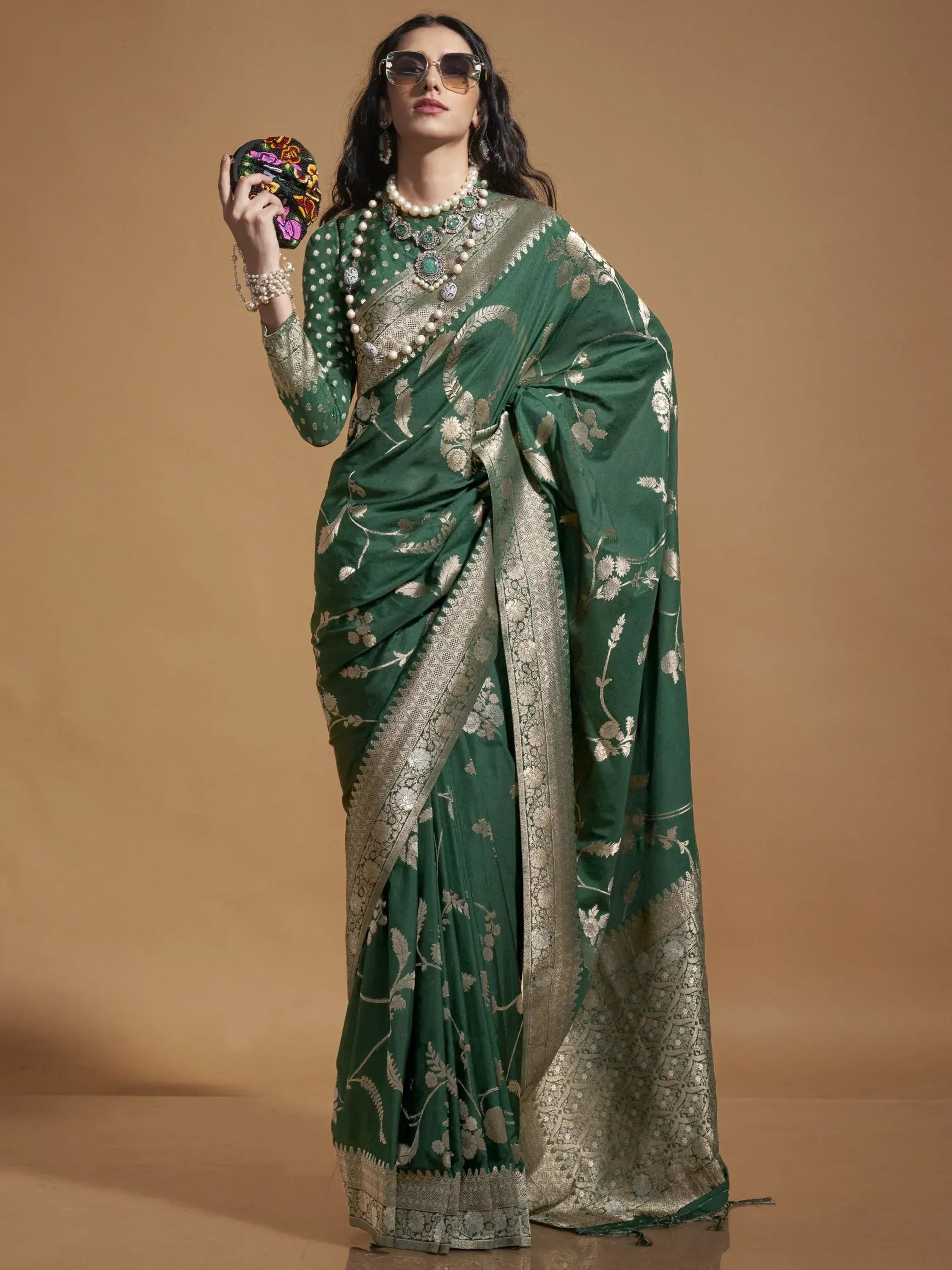 Emerald green saree with gold floral embroidery and heavy border, paired with pearl jewelry and embroidered clutch