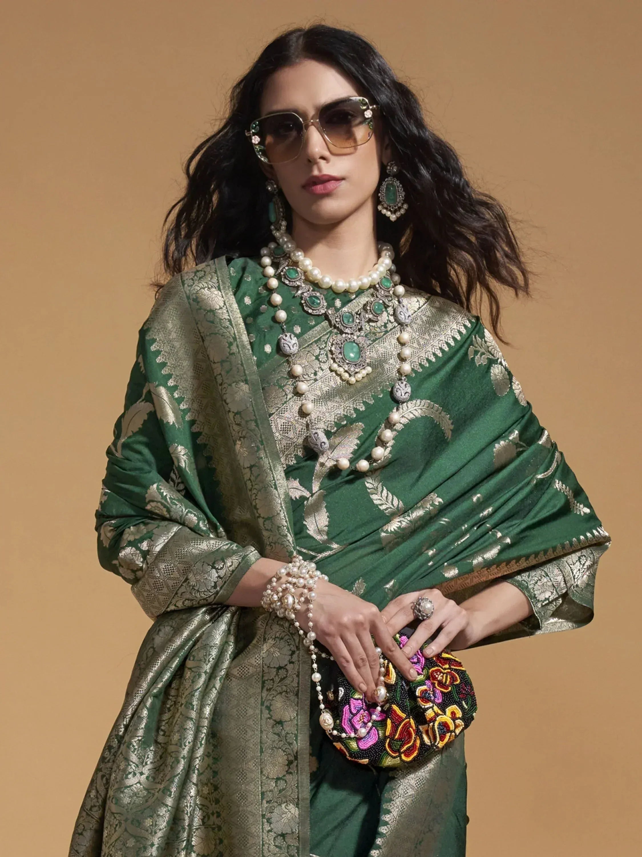 Elegant green ethnic saree with gold embroidery, pearl jewelry, and floral clutch for festive occasions.