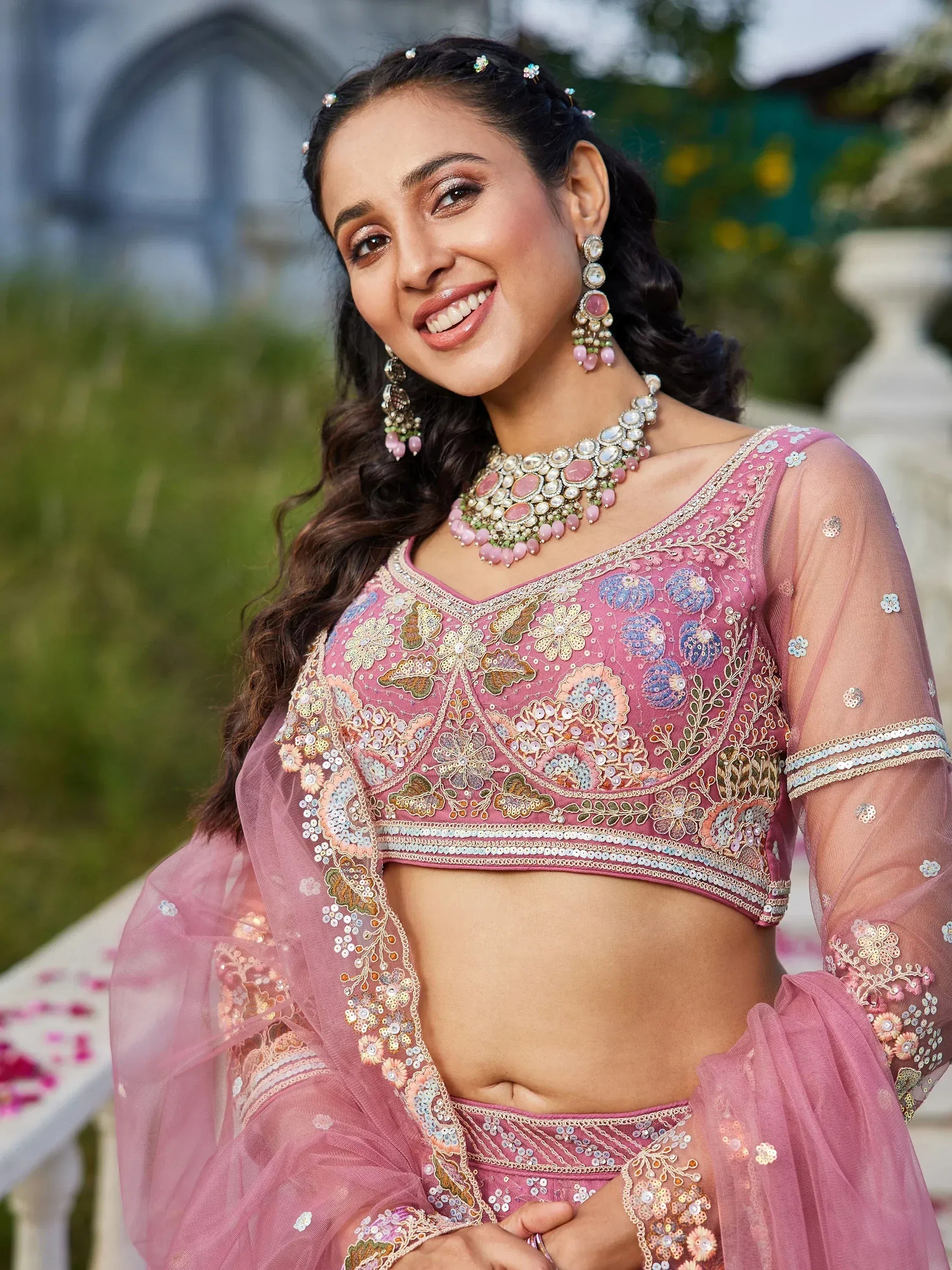 Pink embroidered lehenga choli with floral sequin work, sheer sleeves, and matching jewelry for Indian ethnic wear