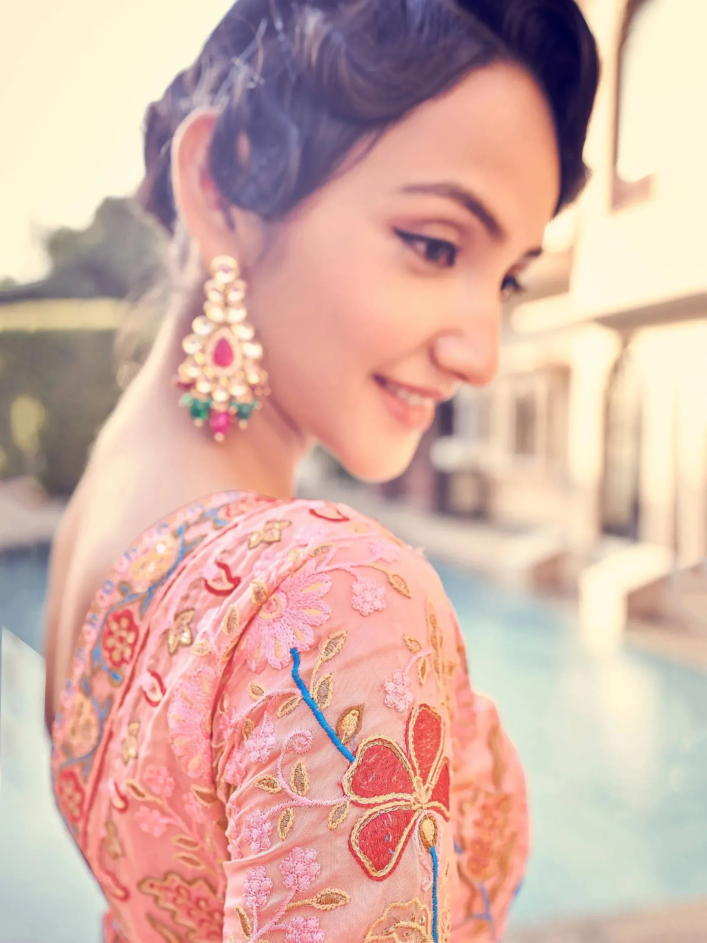 Woman in pink embroidered ethnic gown with floral details and statement earrings, poolside