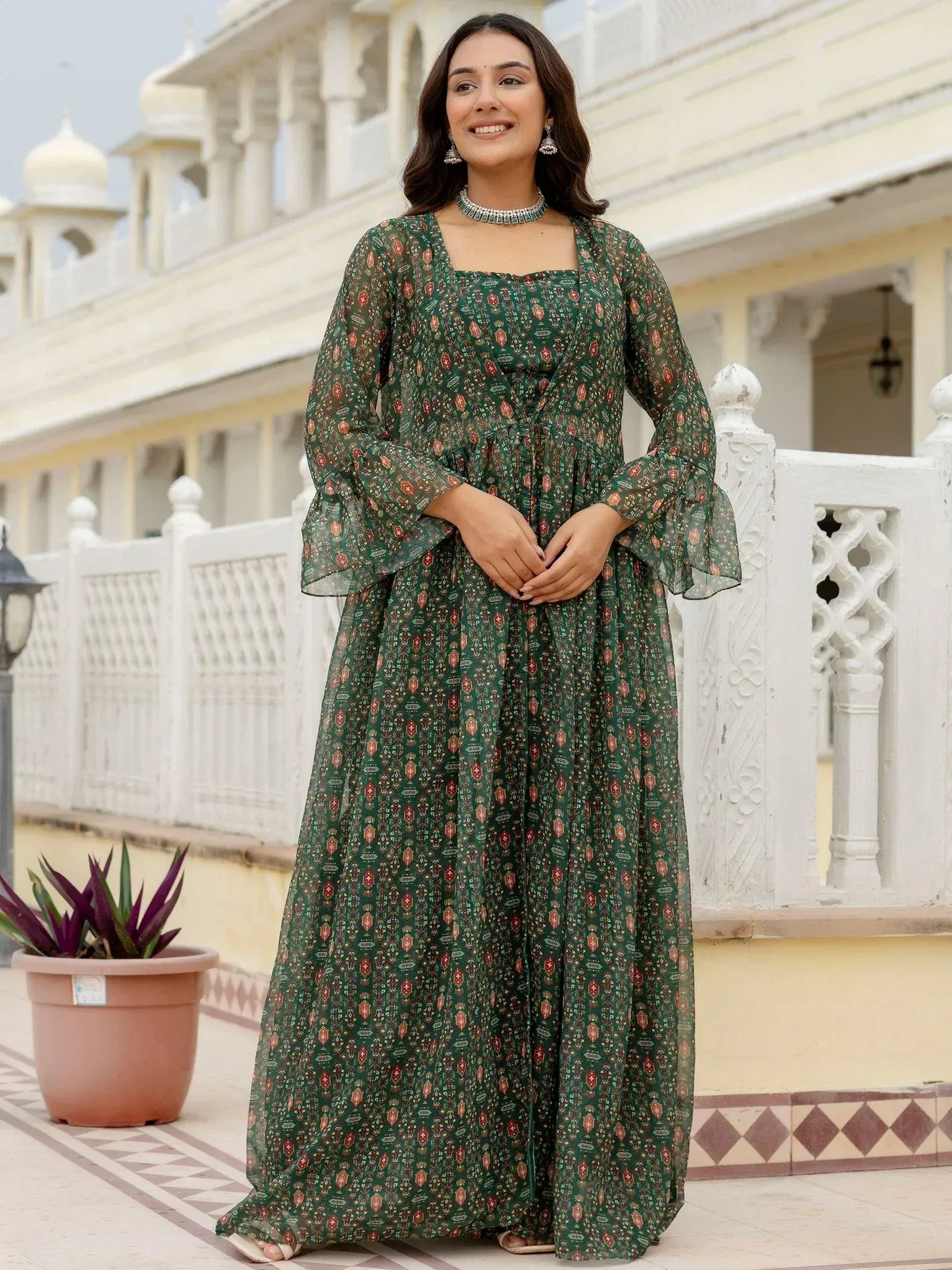 Woman in green printed ethnic gown with flared sleeves, standing near palace-style architecture