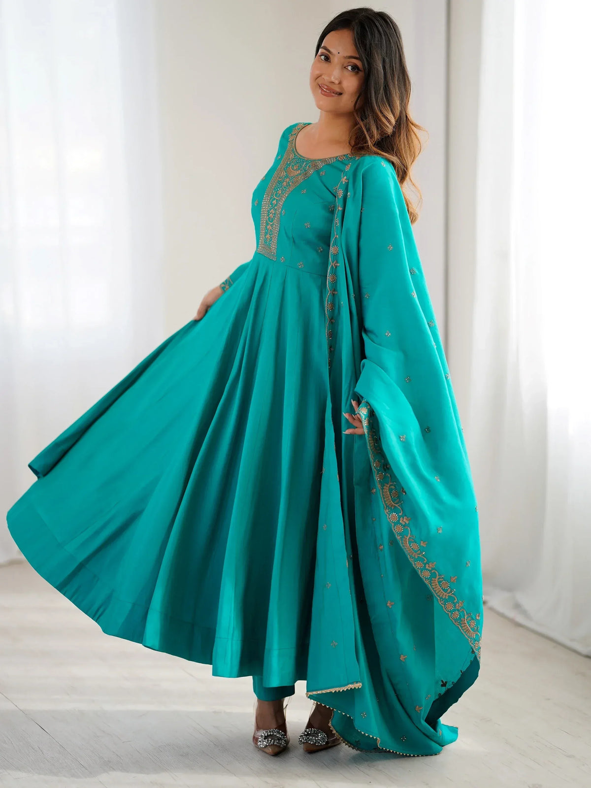 Teal ethnic gown with gold embroidery, flared design, and matching dupatta for festive occasions
