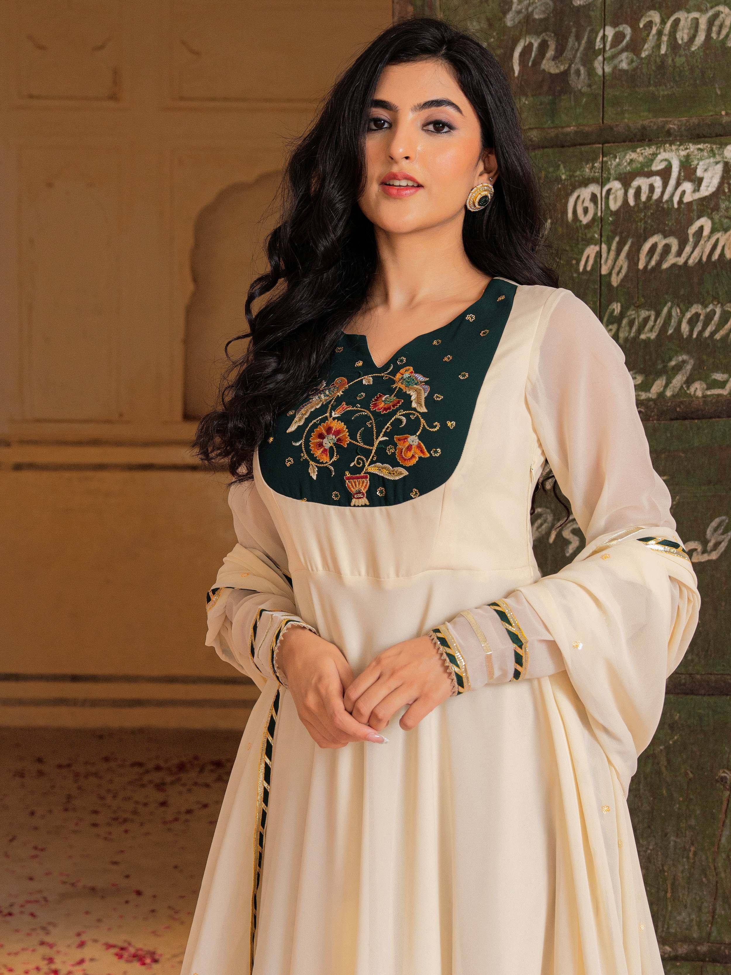 Elegant cream ethnic gown with green floral embroidery and gold detailing, perfect for Indian occasions.