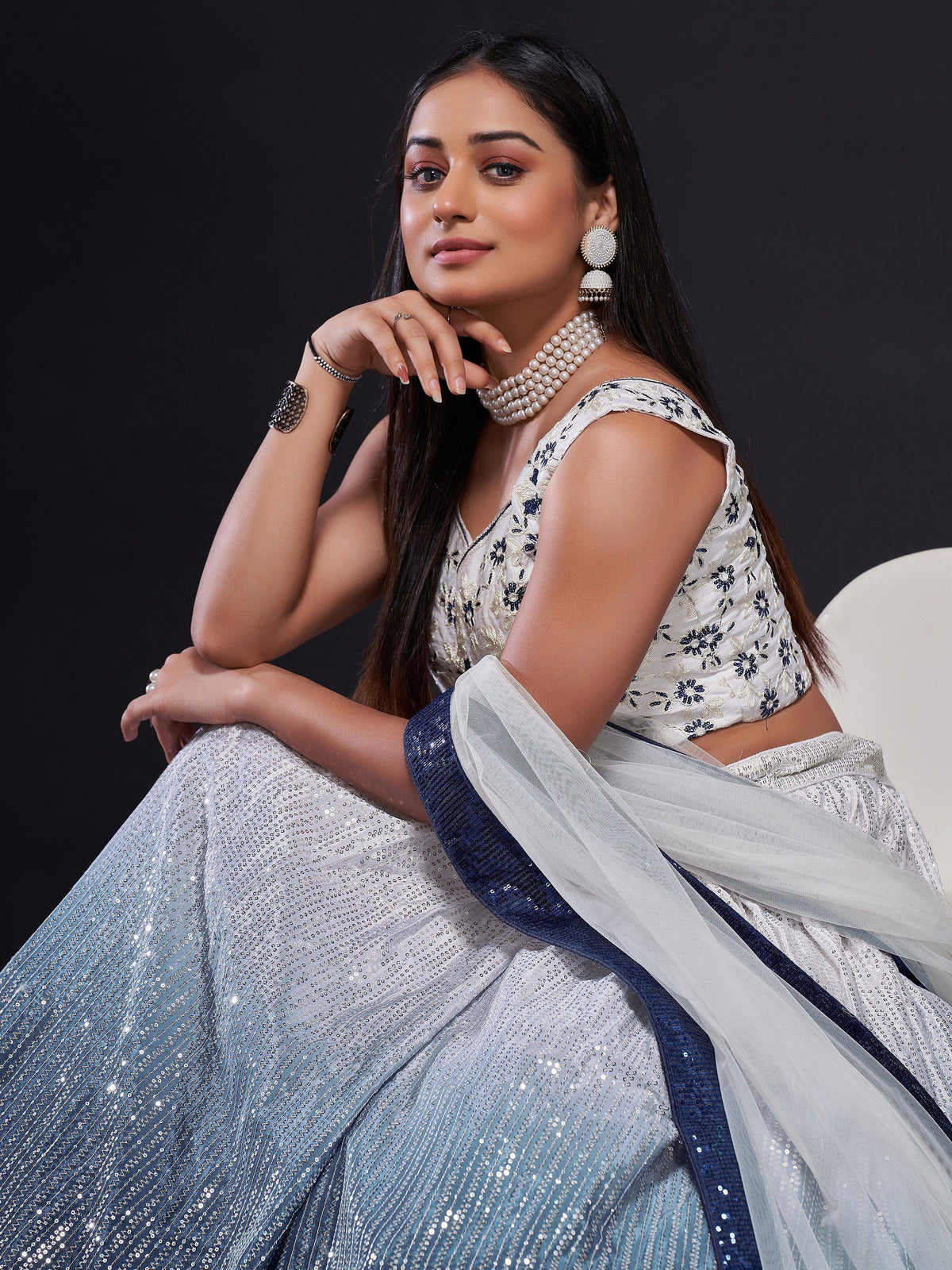 Elegant woman in white and blue embroidered lehenga choli with pearl jewelry, perfect for Indian ethnic wear.