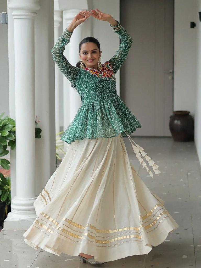 Woman in green printed peplum top with embroidered neckline and cream pleated skirt with gold trim, dancing gracefully
